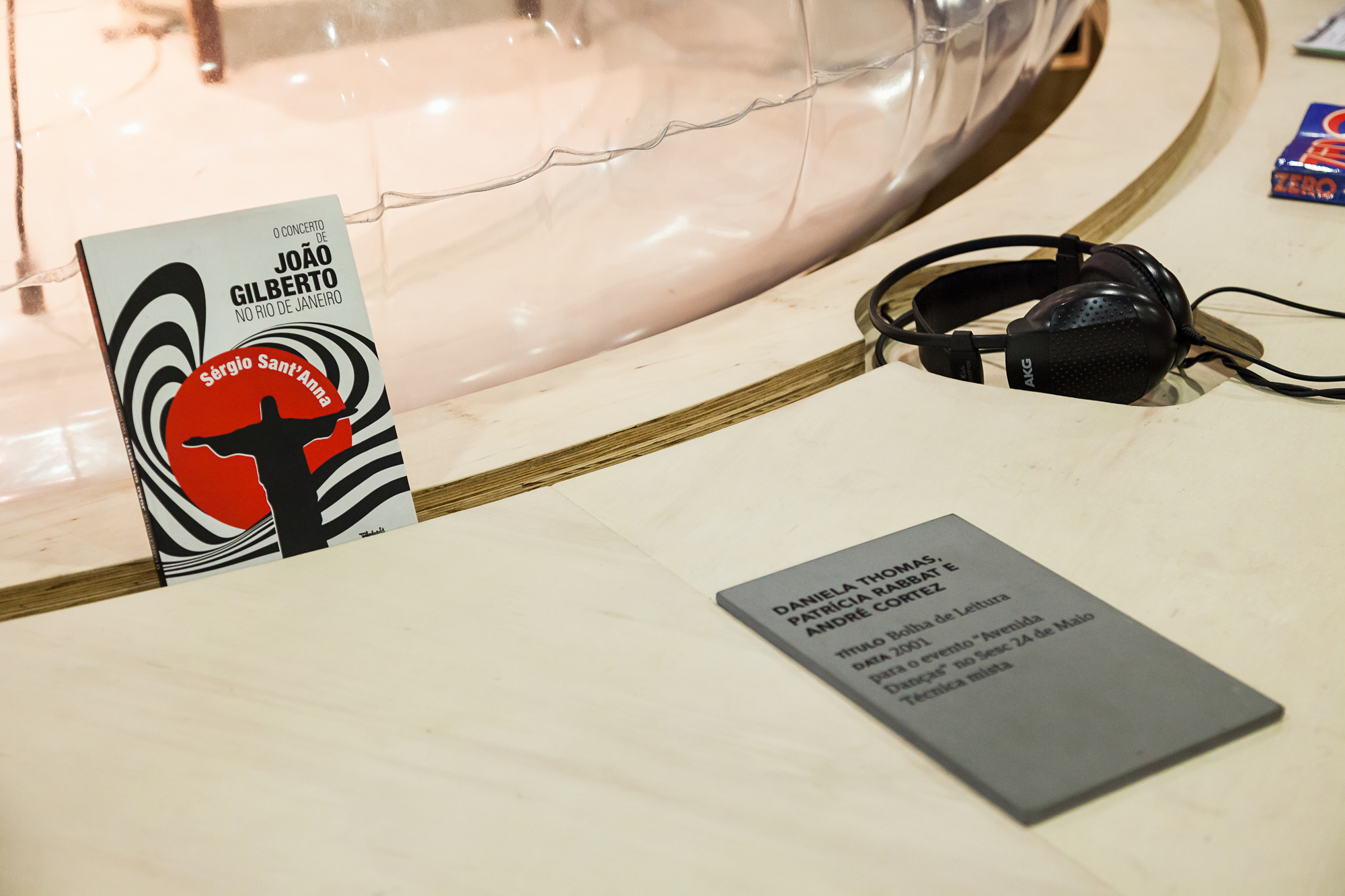 Detail of the wooden reading table with a paperback book, black headphones and a grey engraved label beside the inflatable base