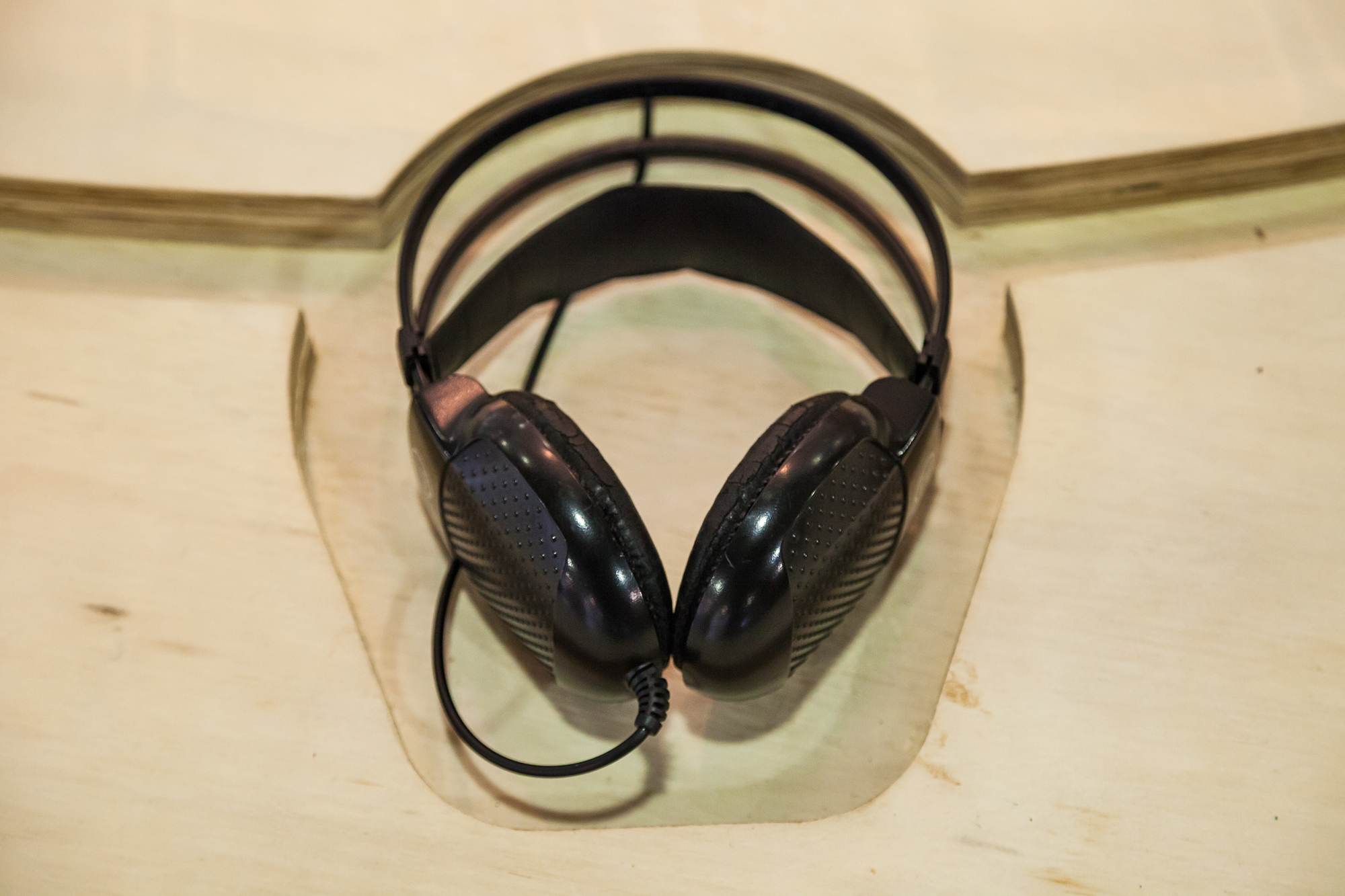 Black over-ear headphones with perforated ear pads resting in a routed recess of a plywood tabletop