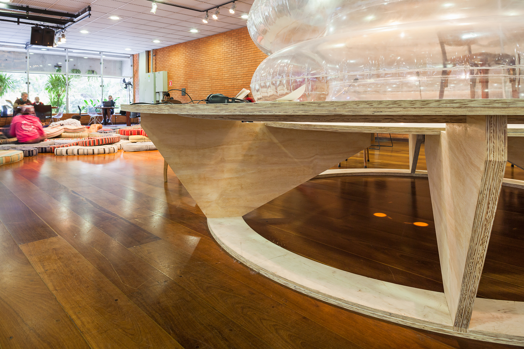 Low angle of the layered plywood base of the round table over a polished timber floor, with floor cushions behind