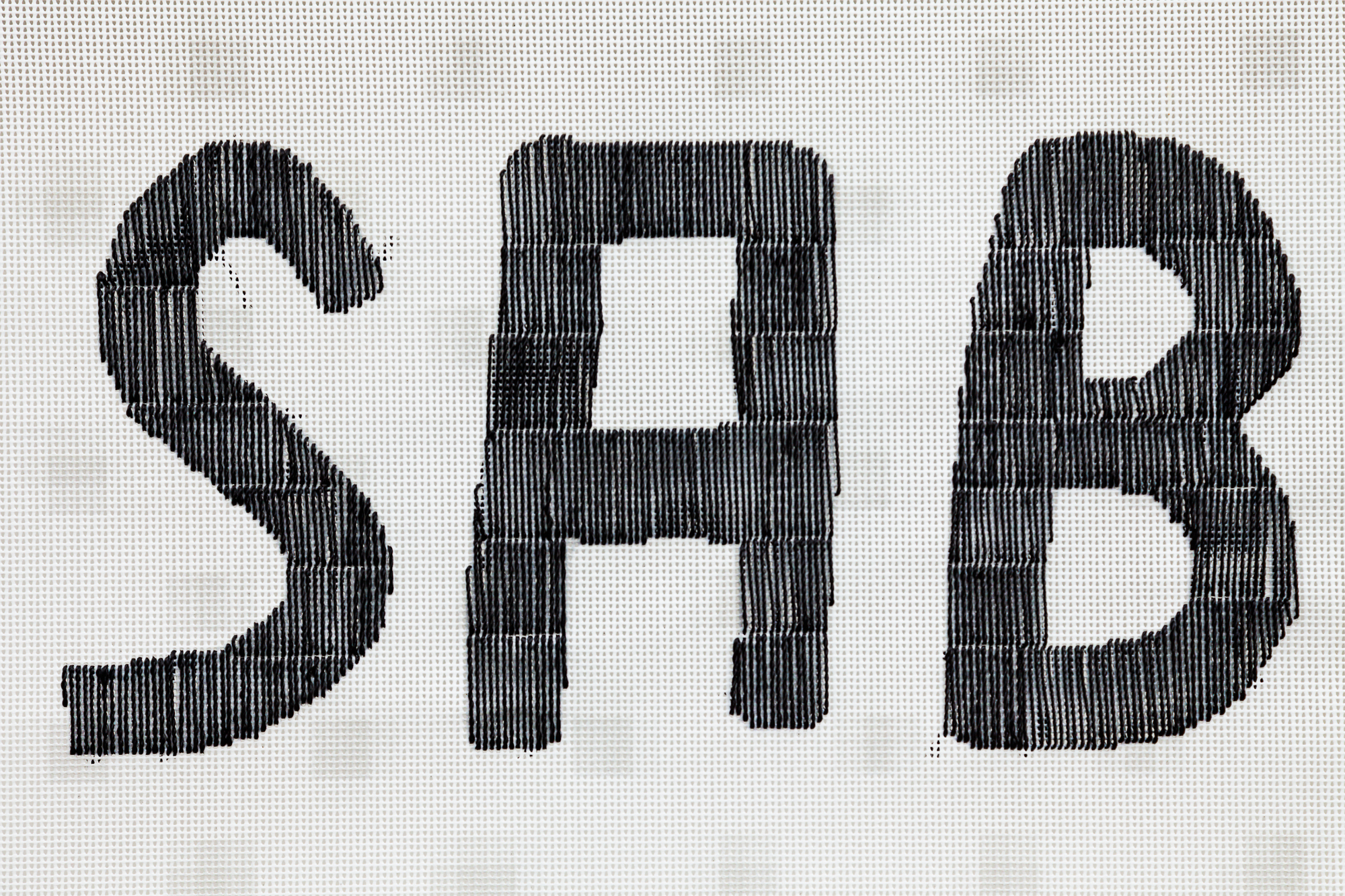 Close-up of the bold black letters S, A and B stitched in vertical thread lines on a white mesh grid