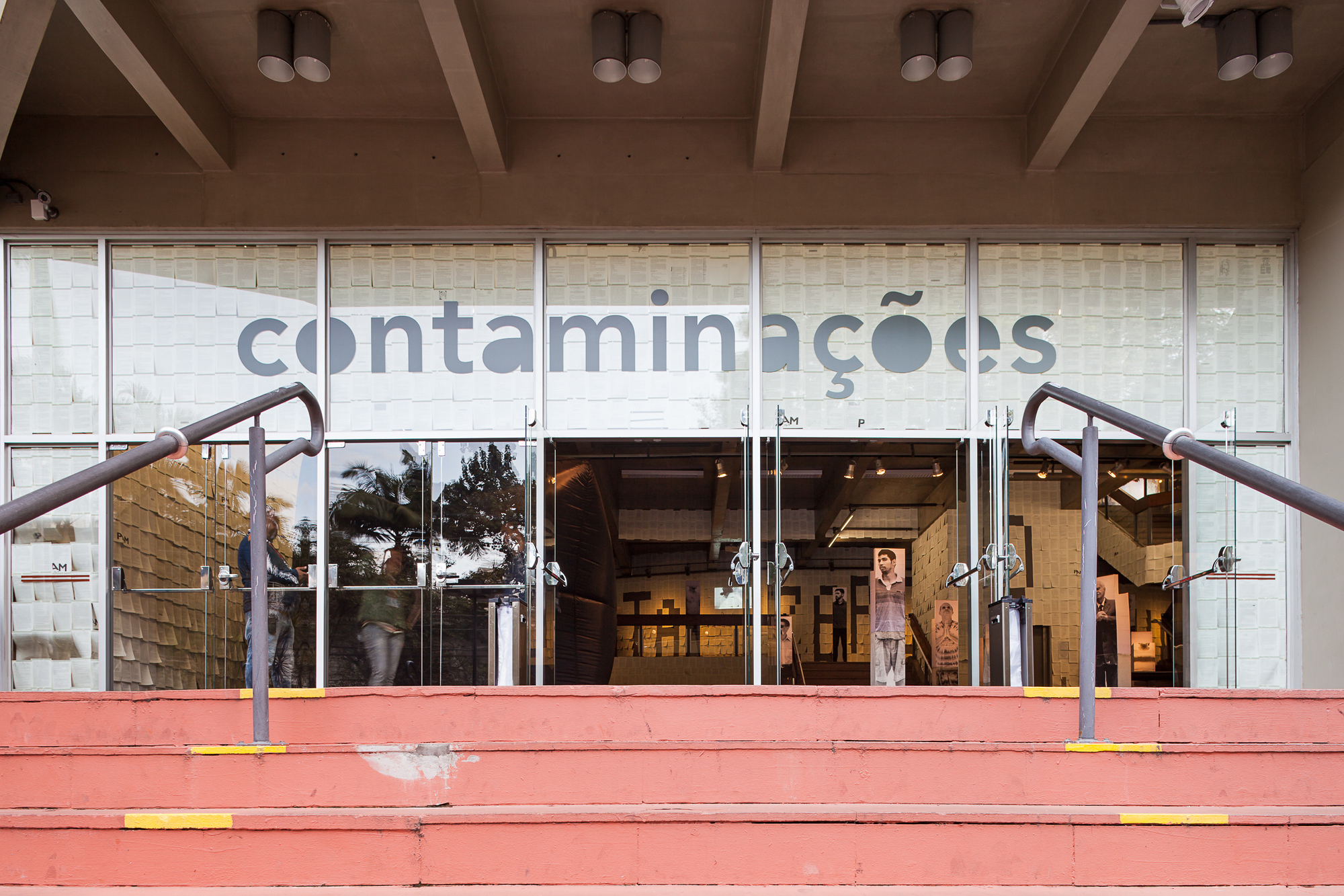 Glazed entrance with large lettering on the glass, steel handrails and pink-painted steps leading up to the doors