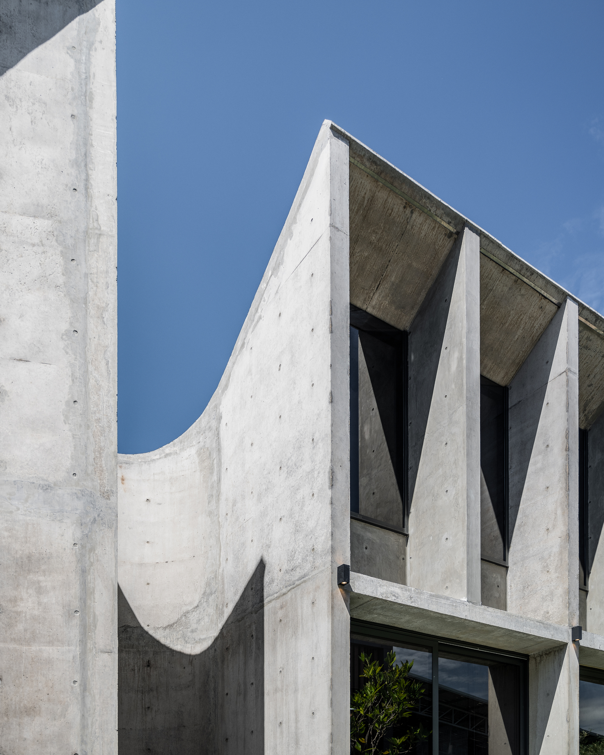 Concrete wall with a scooped curved cutout beside tapered fins and a cantilevered ledge under a clear blue sky