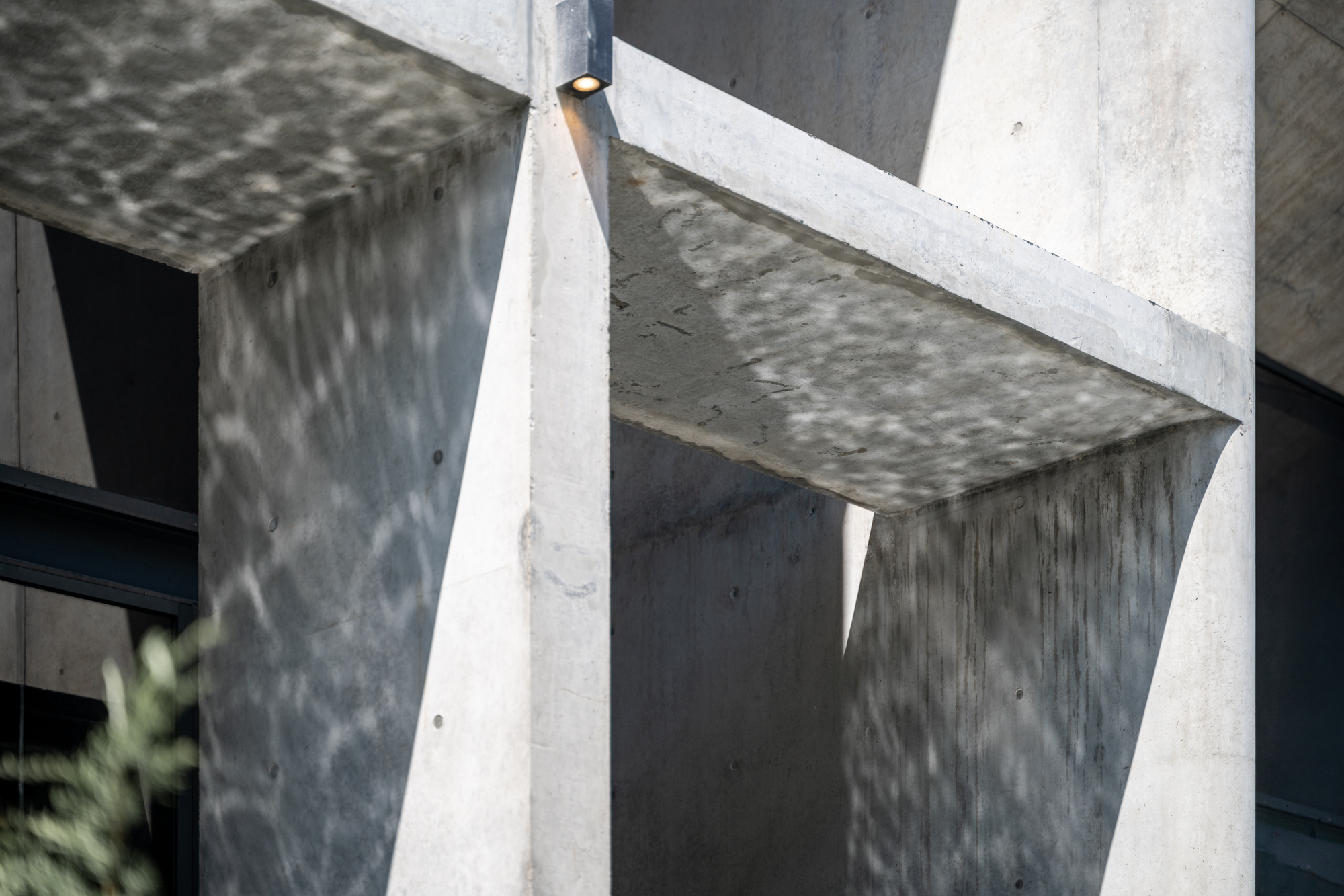Close-up of concrete beams and tapered columns with dappled water reflections on the soffit and a small downlight