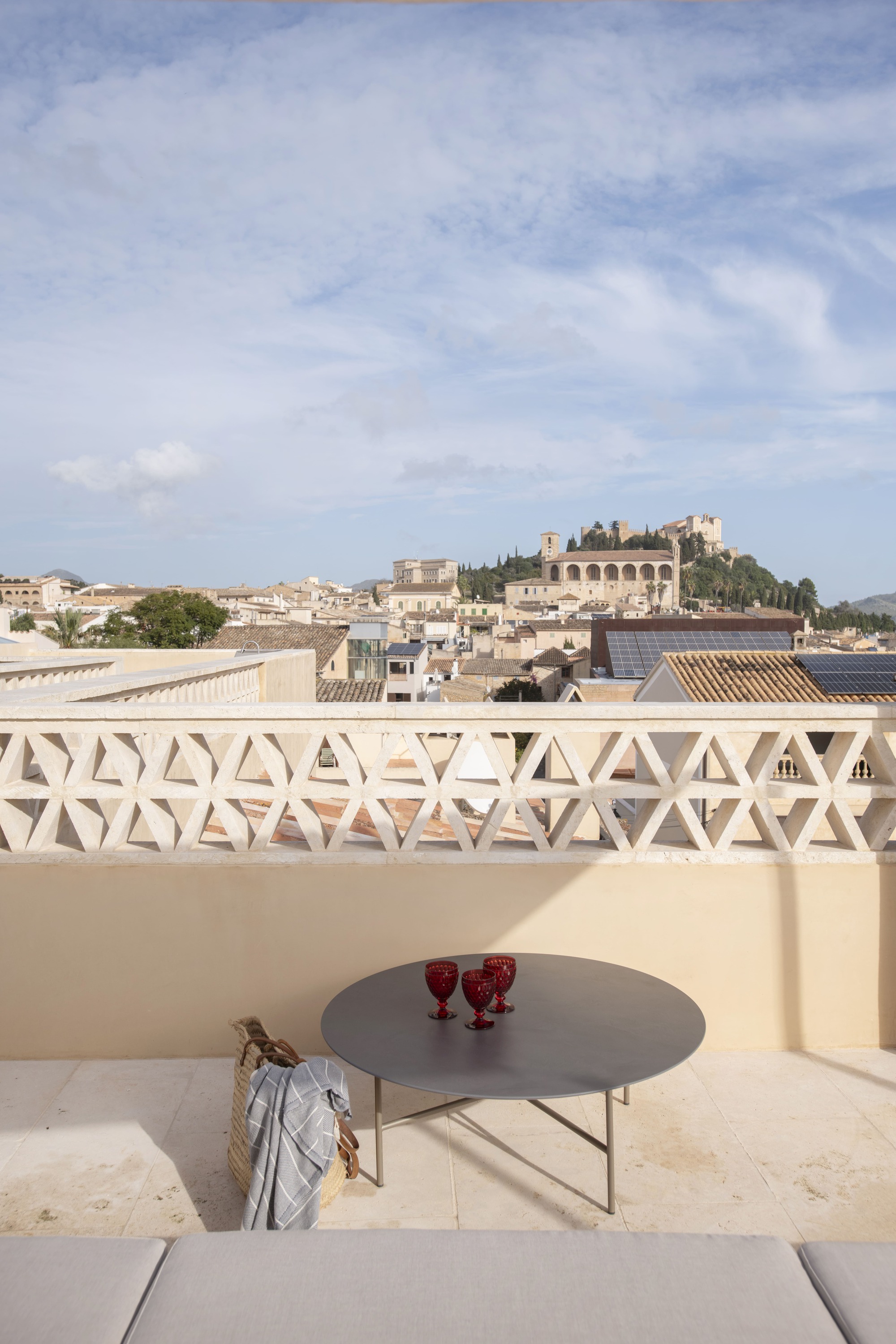 Roof terrace with lattice parapet, round table with red glasses and a view over tiled rooftops toward a hilltop church