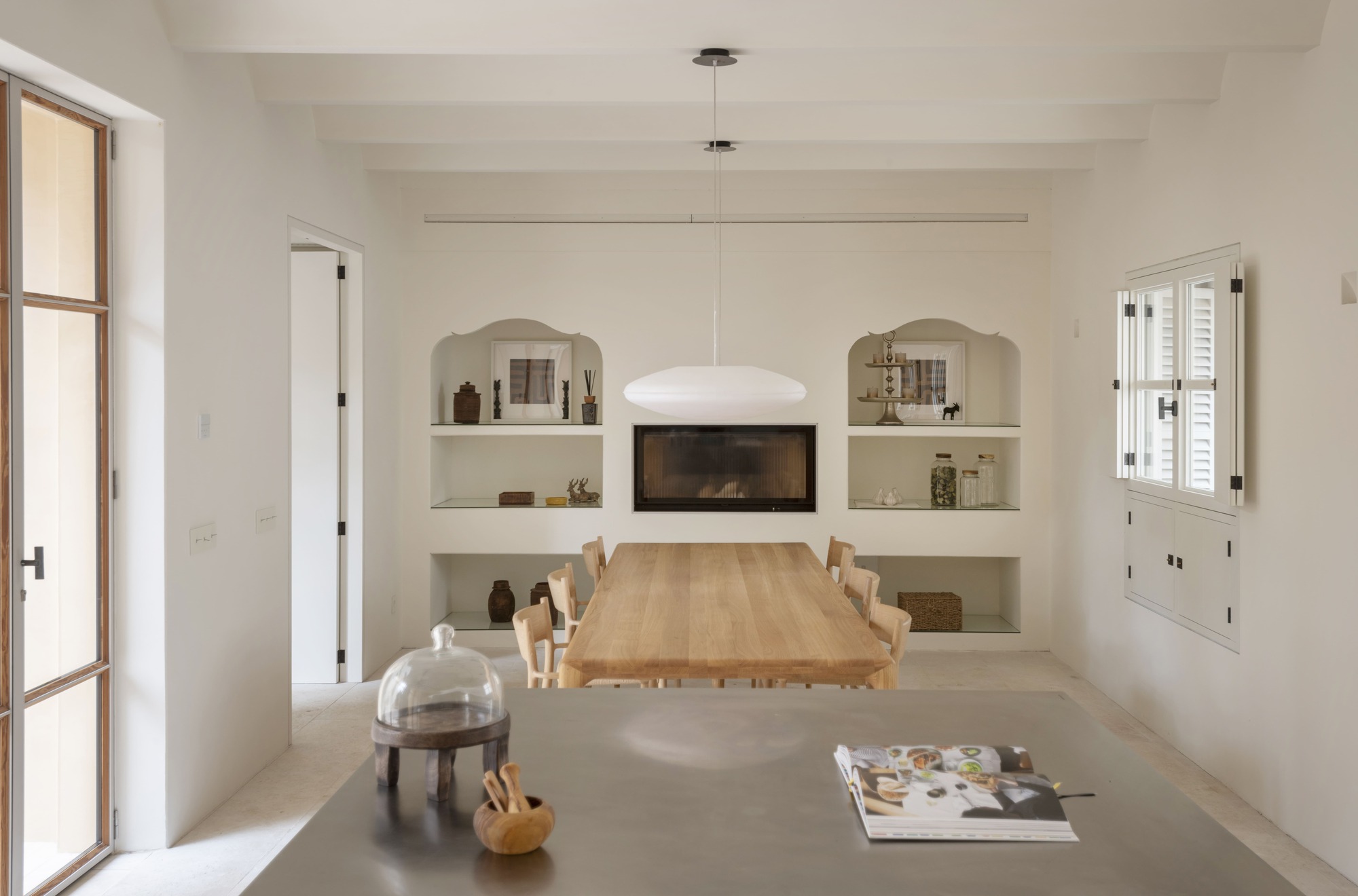 Dining room with a long oak table, arched wall niches and a recessed fireplace beneath a white pendant lamp