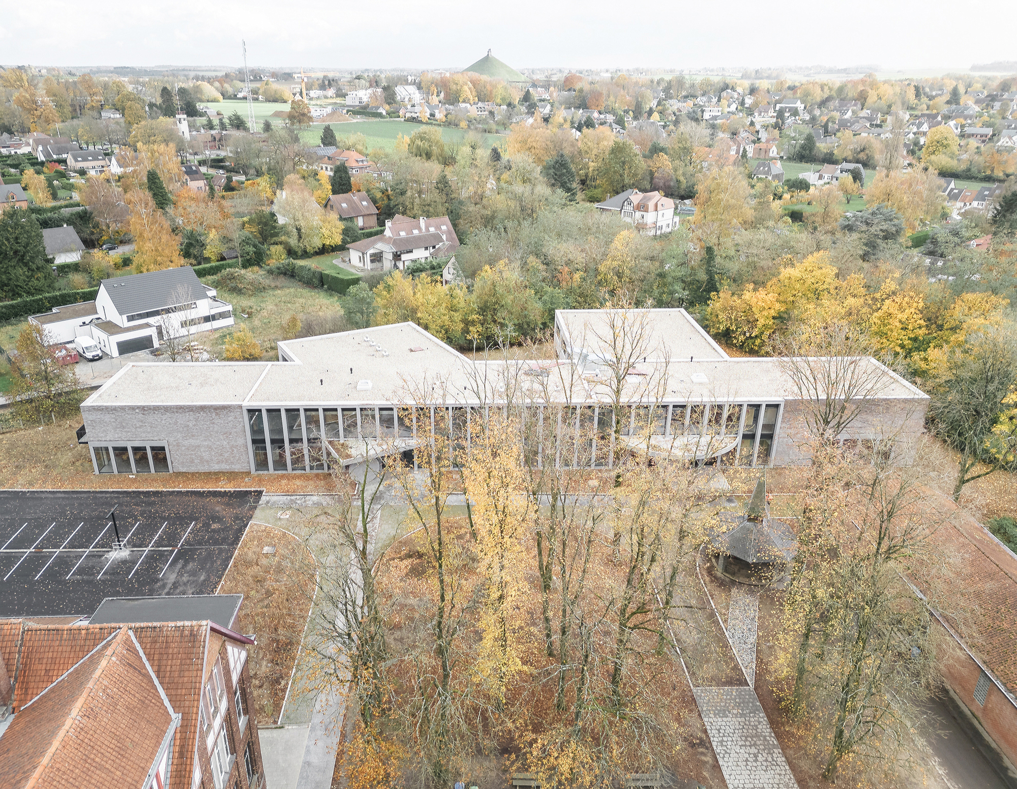 Drone view of the flat-roofed brick and glass school building among yellowing trees, with a chapel roof and houses beyond