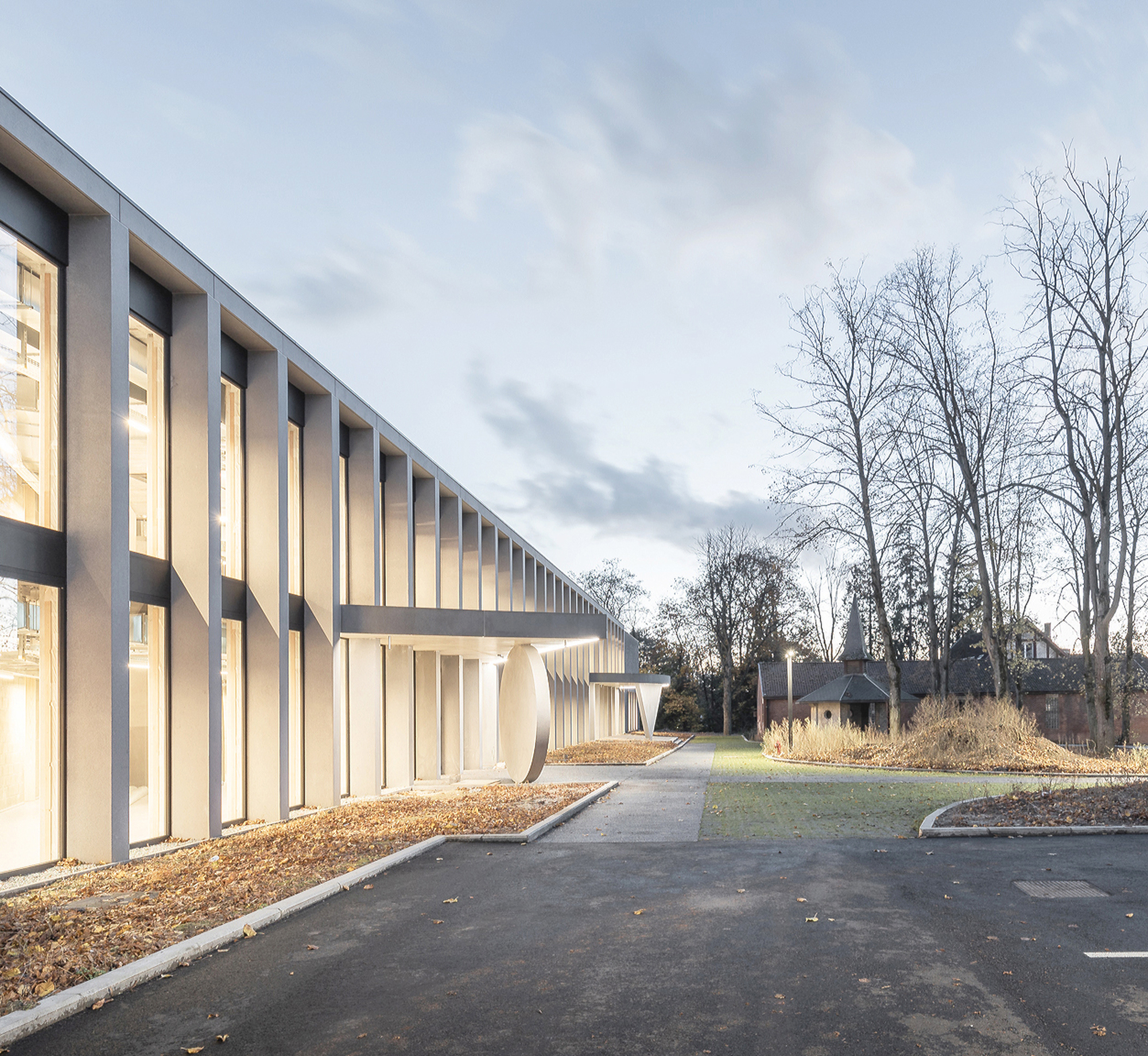 Receding facade of slender grey columns and glass beside a paved path leading to the chapel at dusk