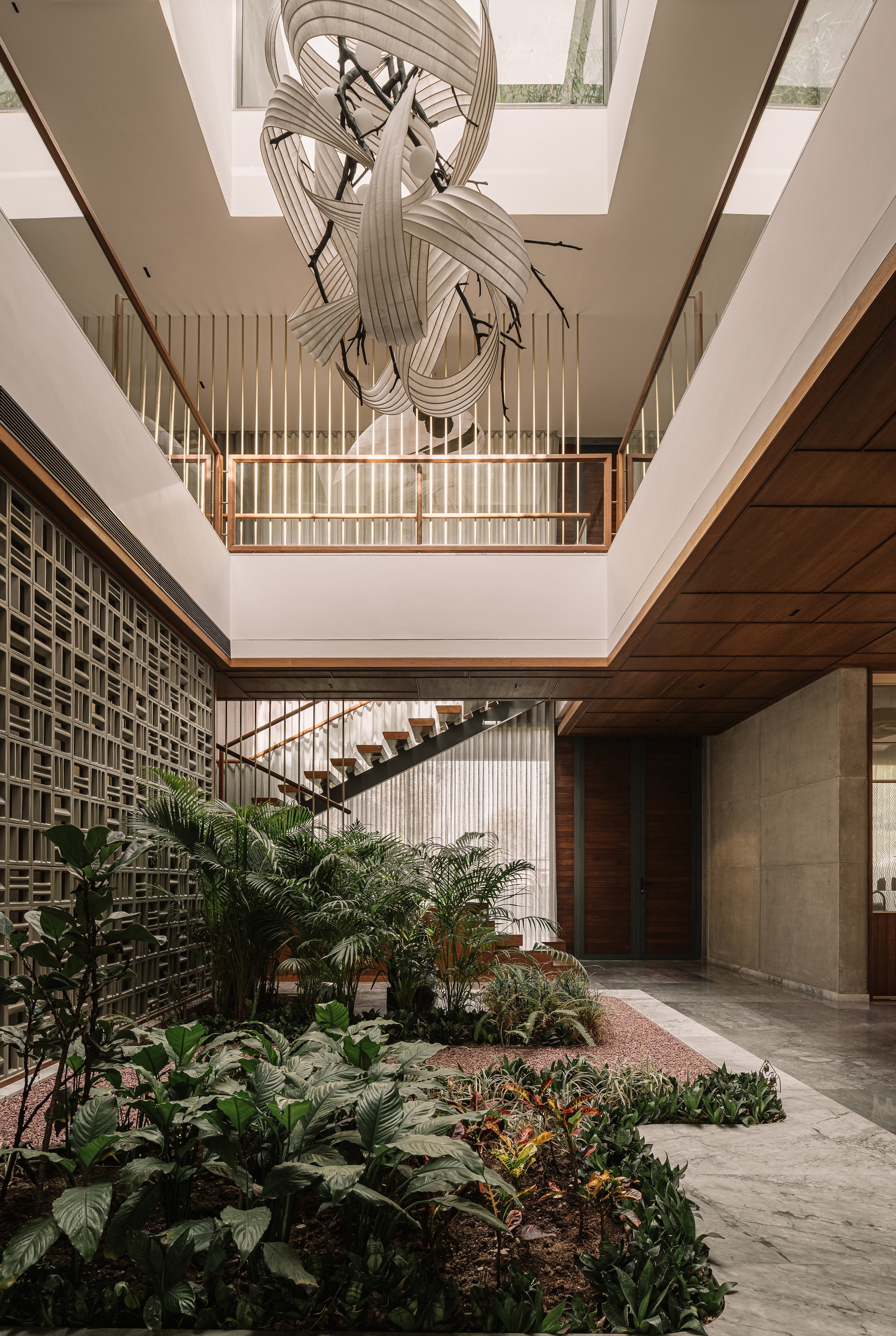Double-height atrium with a sculptural hanging light, perforated concrete screen wall and planted bed, daylight falling from a skylight above