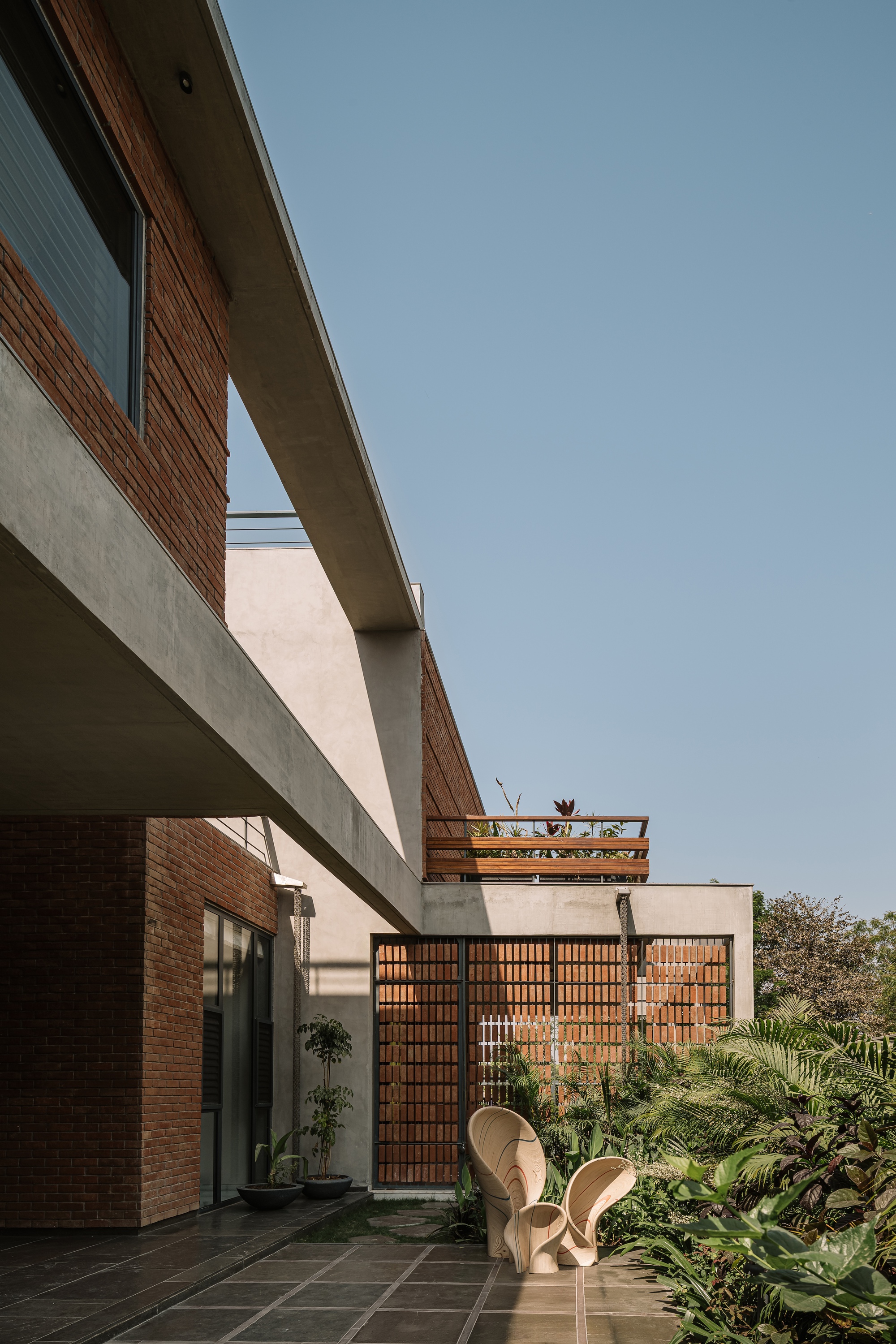 Side courtyard beneath a concrete overhang with brick walls, a lattice brick screen and two woven lounge chairs among ferns