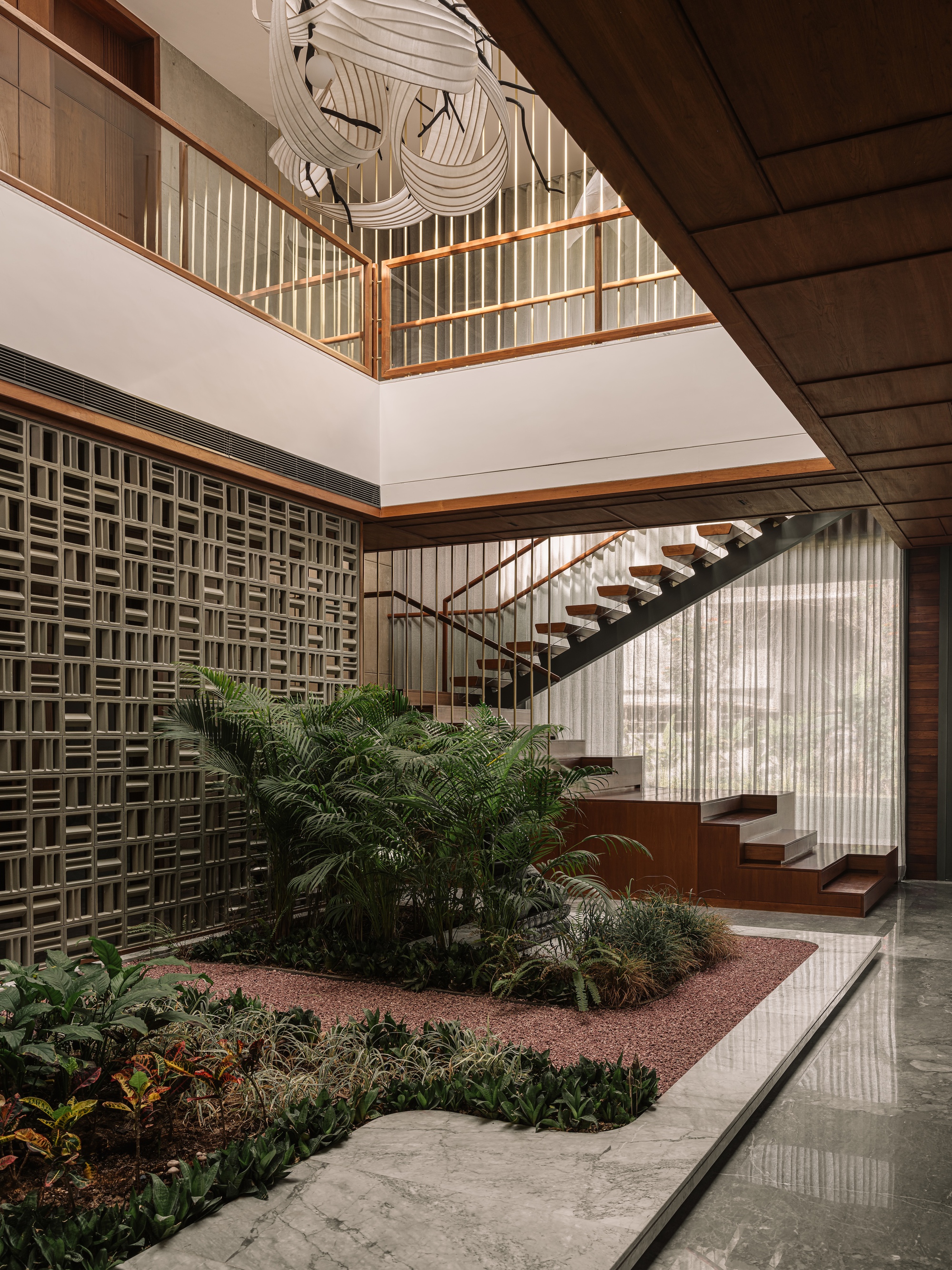Indoor courtyard with a planted gravel bed, perforated block wall and floating timber stair beneath a woven white pendant light