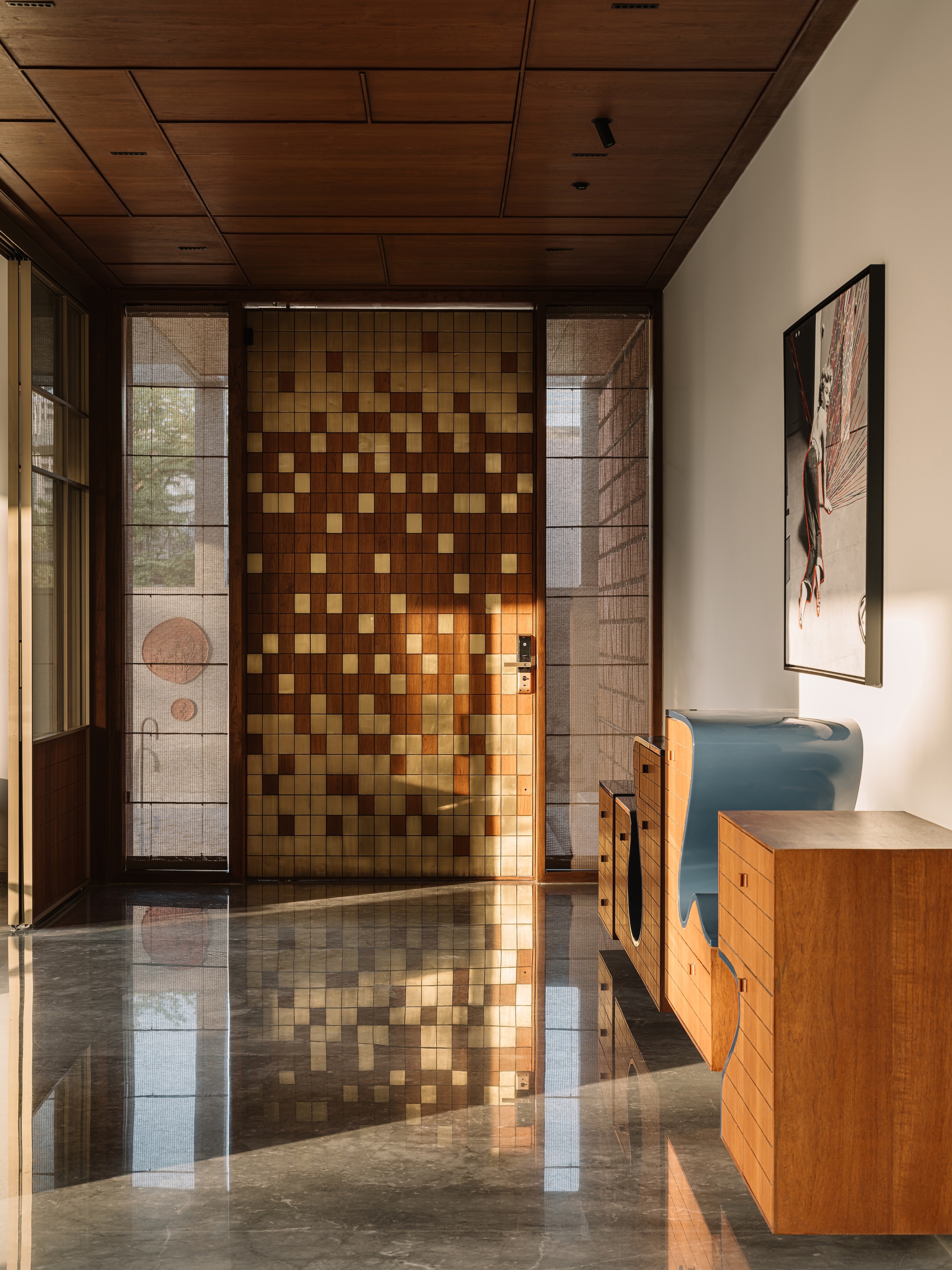 Entrance hall with a checkered wood and brass tile door reflected in the glossy marble floor, a sculptural blue cabinet at right