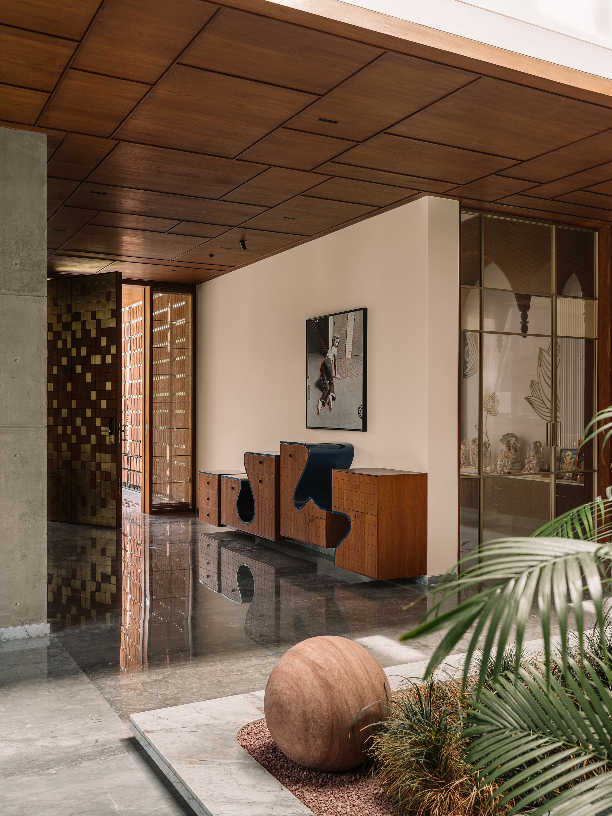 Foyer with sculpted timber cabinets under a coffered wood ceiling, a round stone sphere set in a planted bed in the foreground