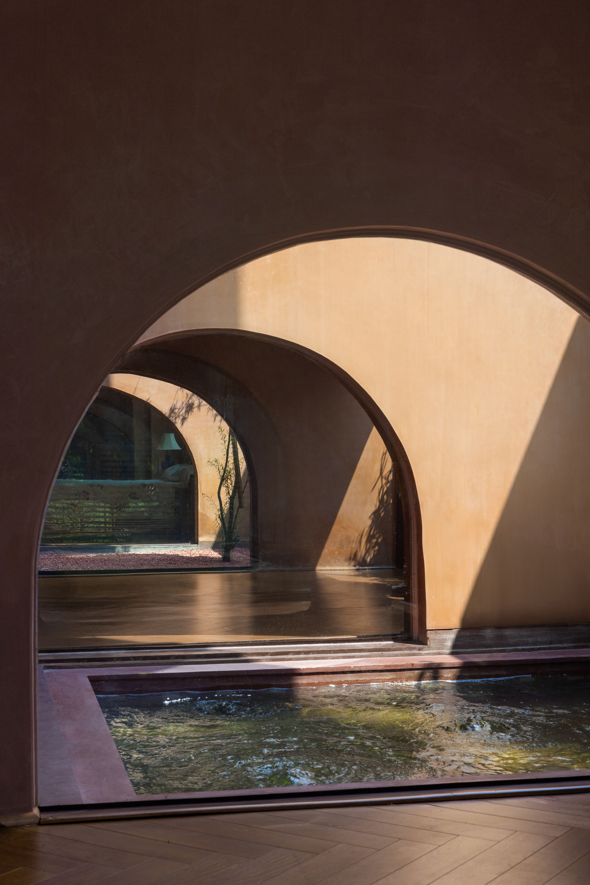 Sequence of arched openings beside a shallow indoor water channel, with sunlight casting diagonal shadows on plastered walls