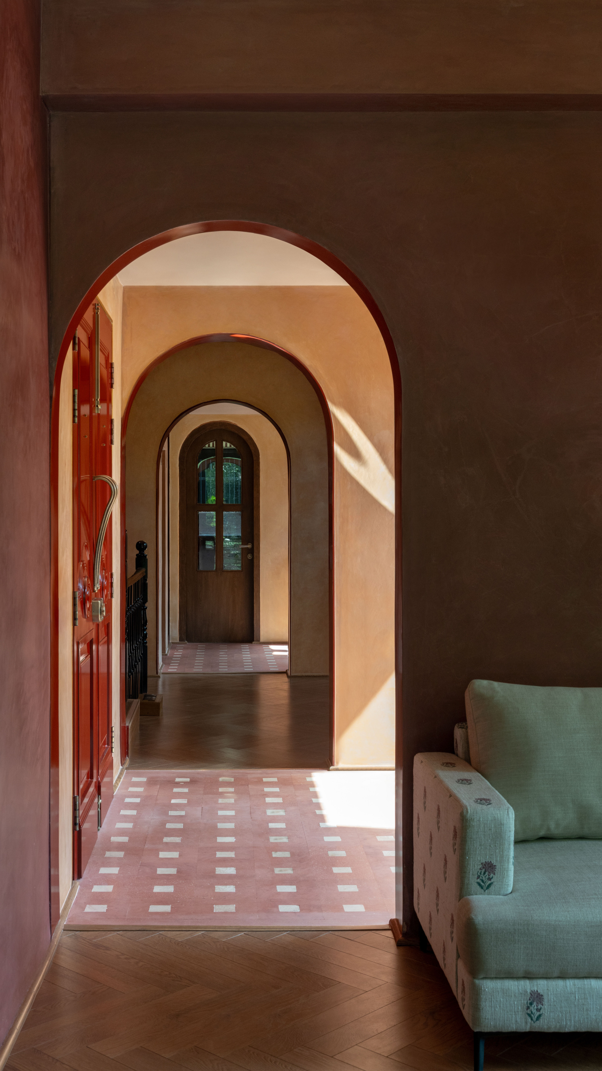 Enfilade of nested arches leading to a glazed timber door, with a patterned tile threshold and sunlight on herringbone flooring