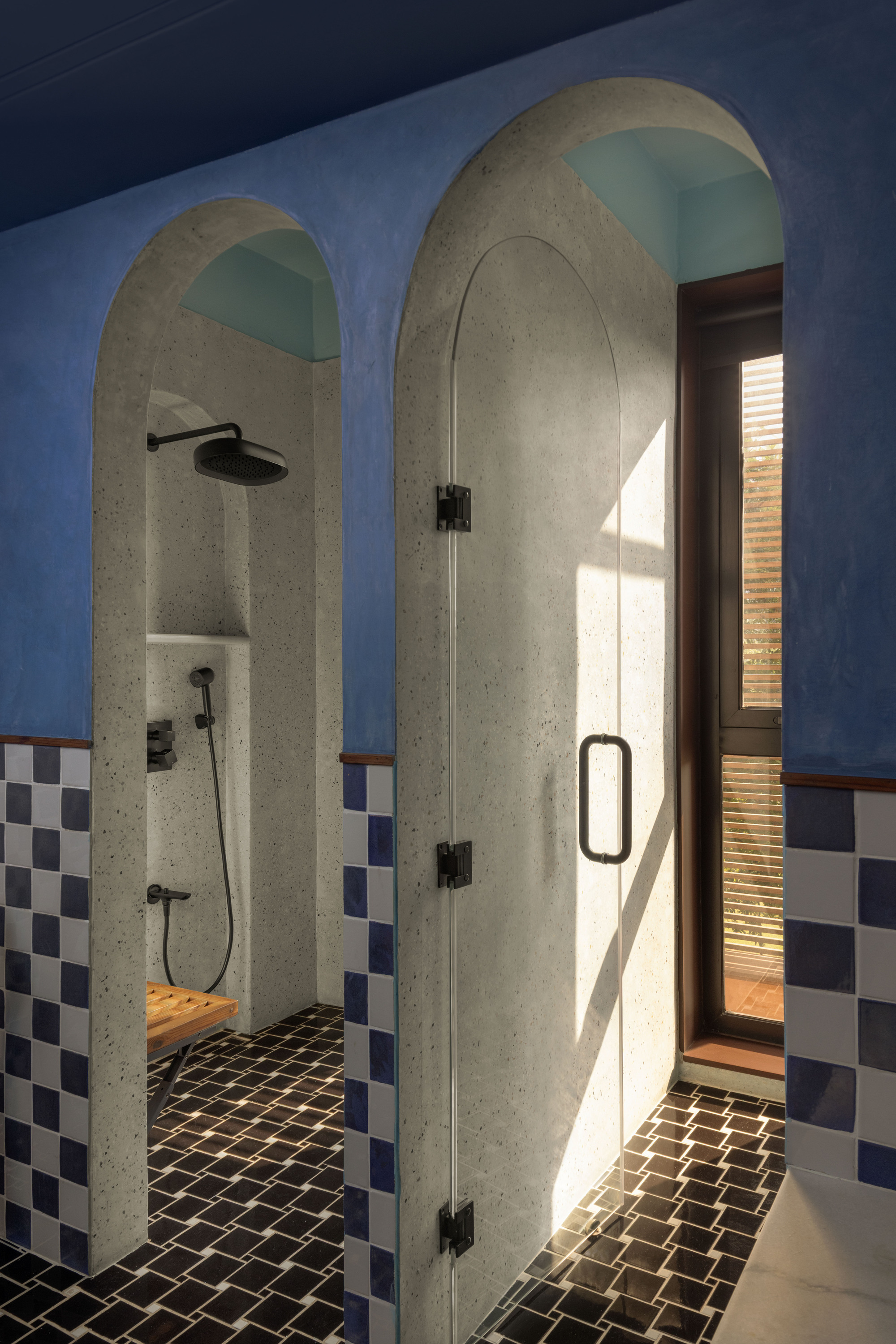 Shower with arched openings in speckled plaster, blue walls and blue-white tile dado, daylight falling through a glass door