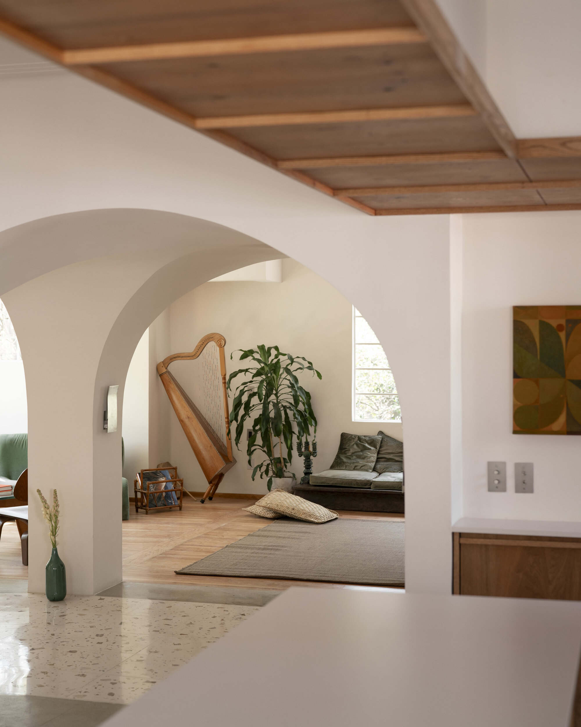 View through plaster arches to a harp, a potted plant and a low daybed, under a timber-framed ceiling soffit