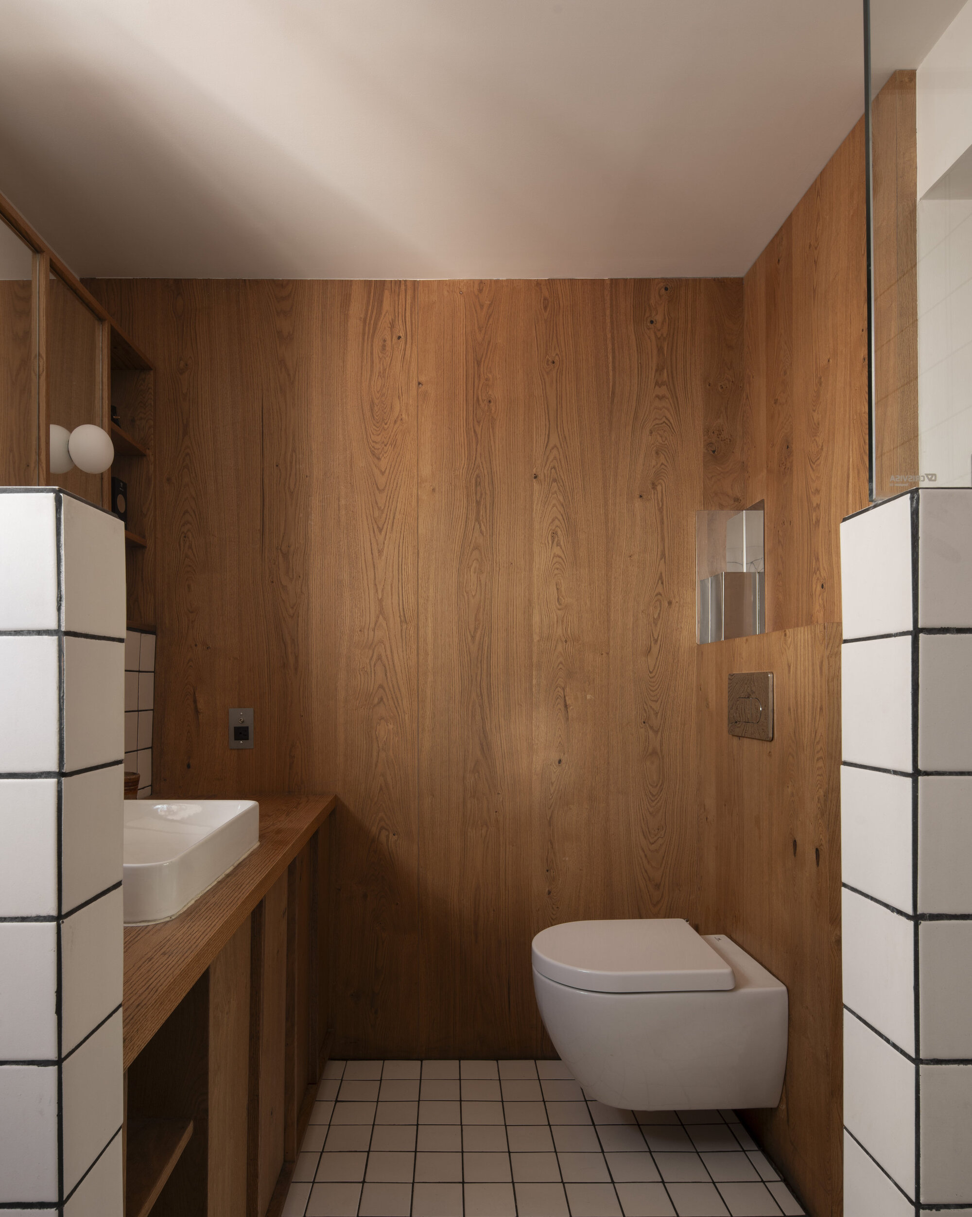 Bathroom with oak plank walls, wall-hung toilet and white square tiles with dark grout flanking a timber vanity
