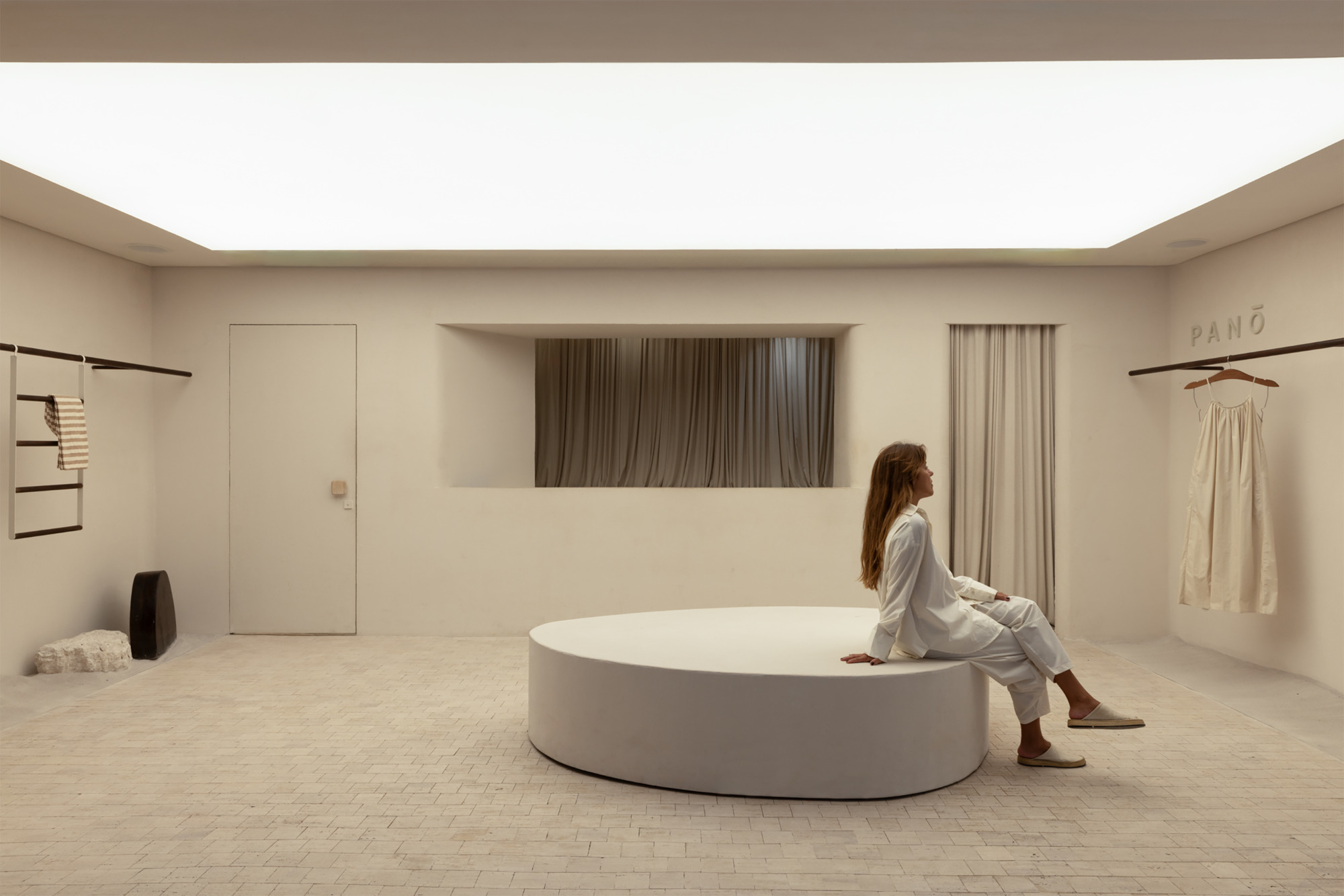 Woman in white seated on a round plaster platform in a boutique lit by a glowing luminous ceiling panel