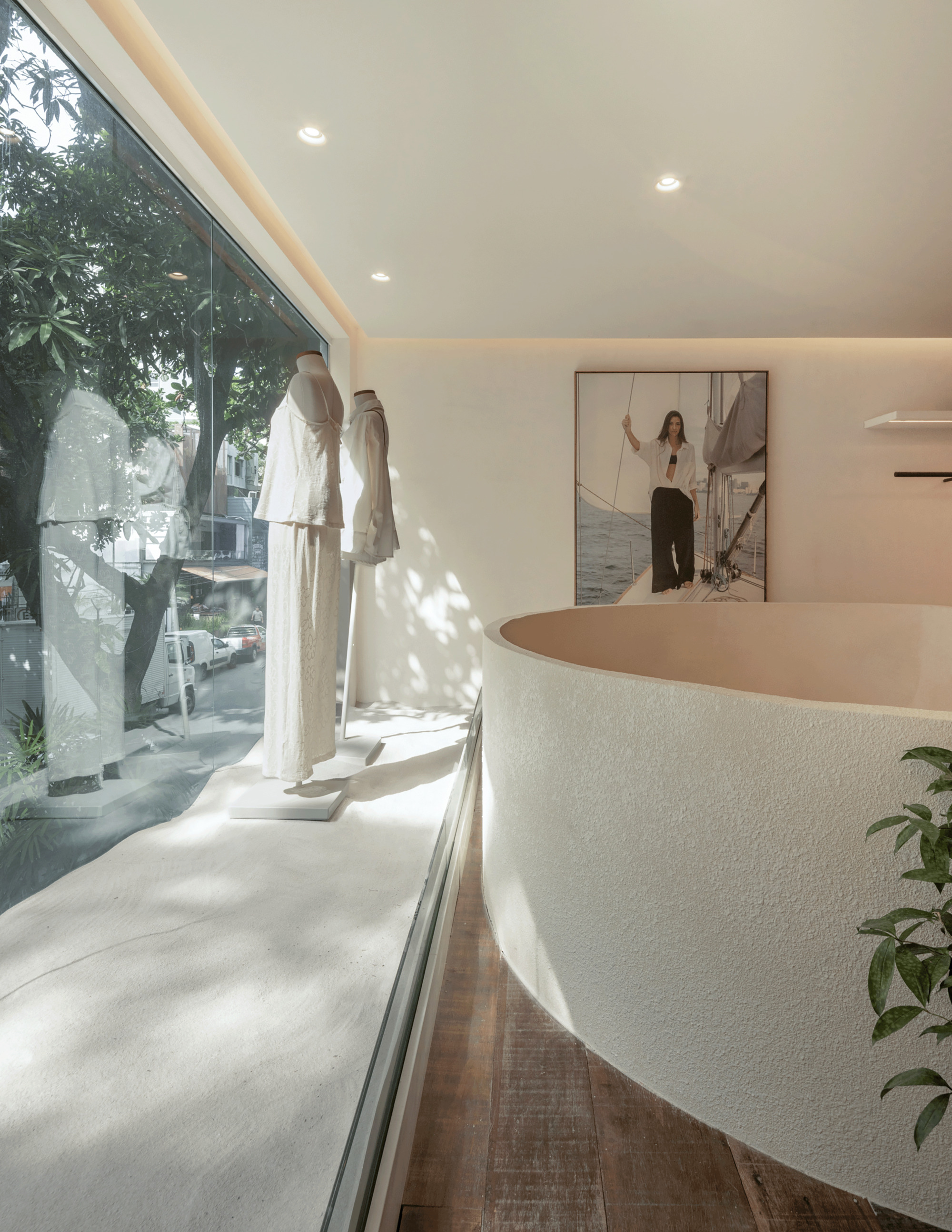 Shop window display with clothed mannequins and a curved textured plaster counter, tree shadows falling across the pale floor