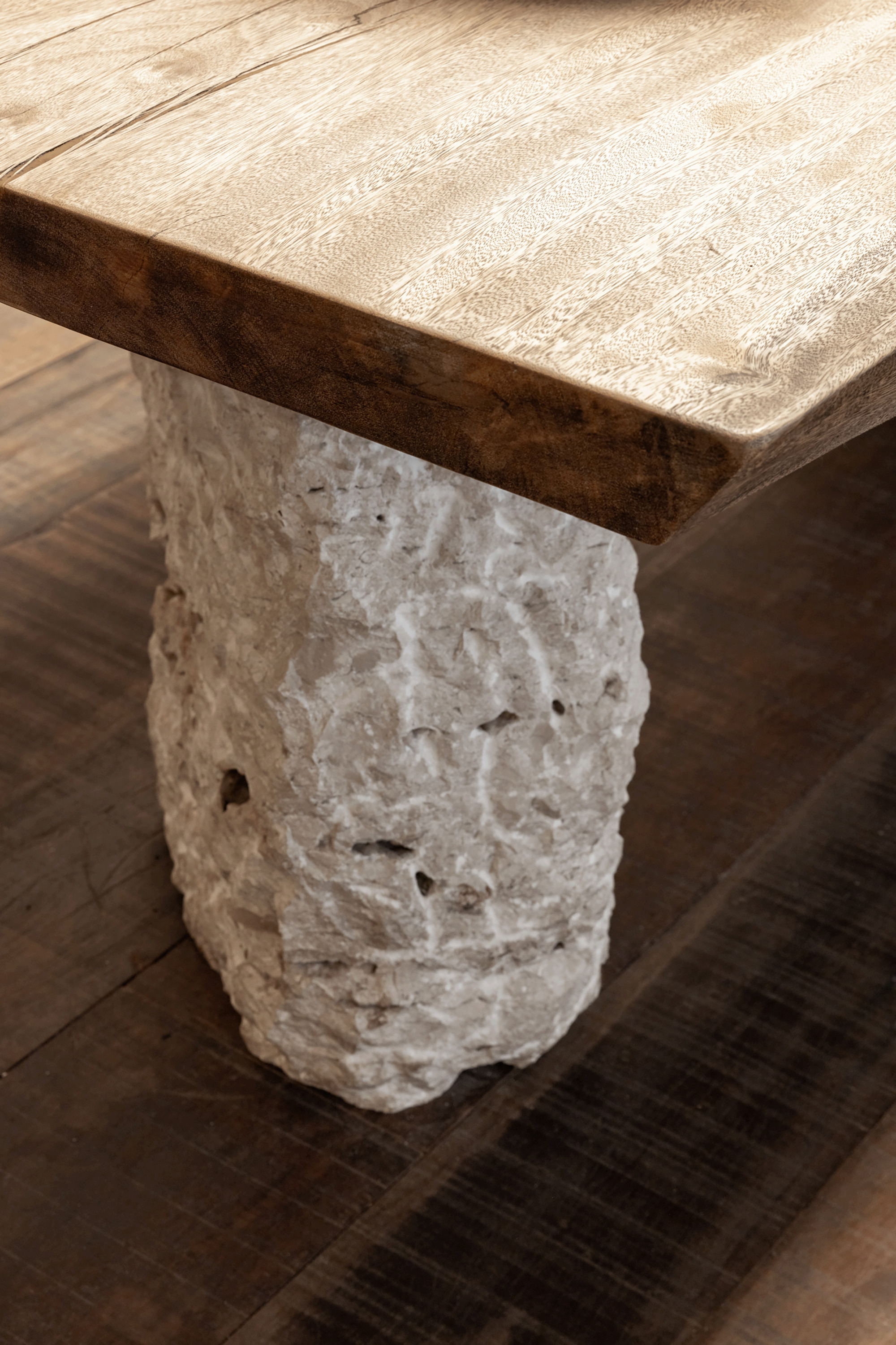 Close-up of a live-edge timber tabletop resting on a rough-hewn stone base over dark plank flooring