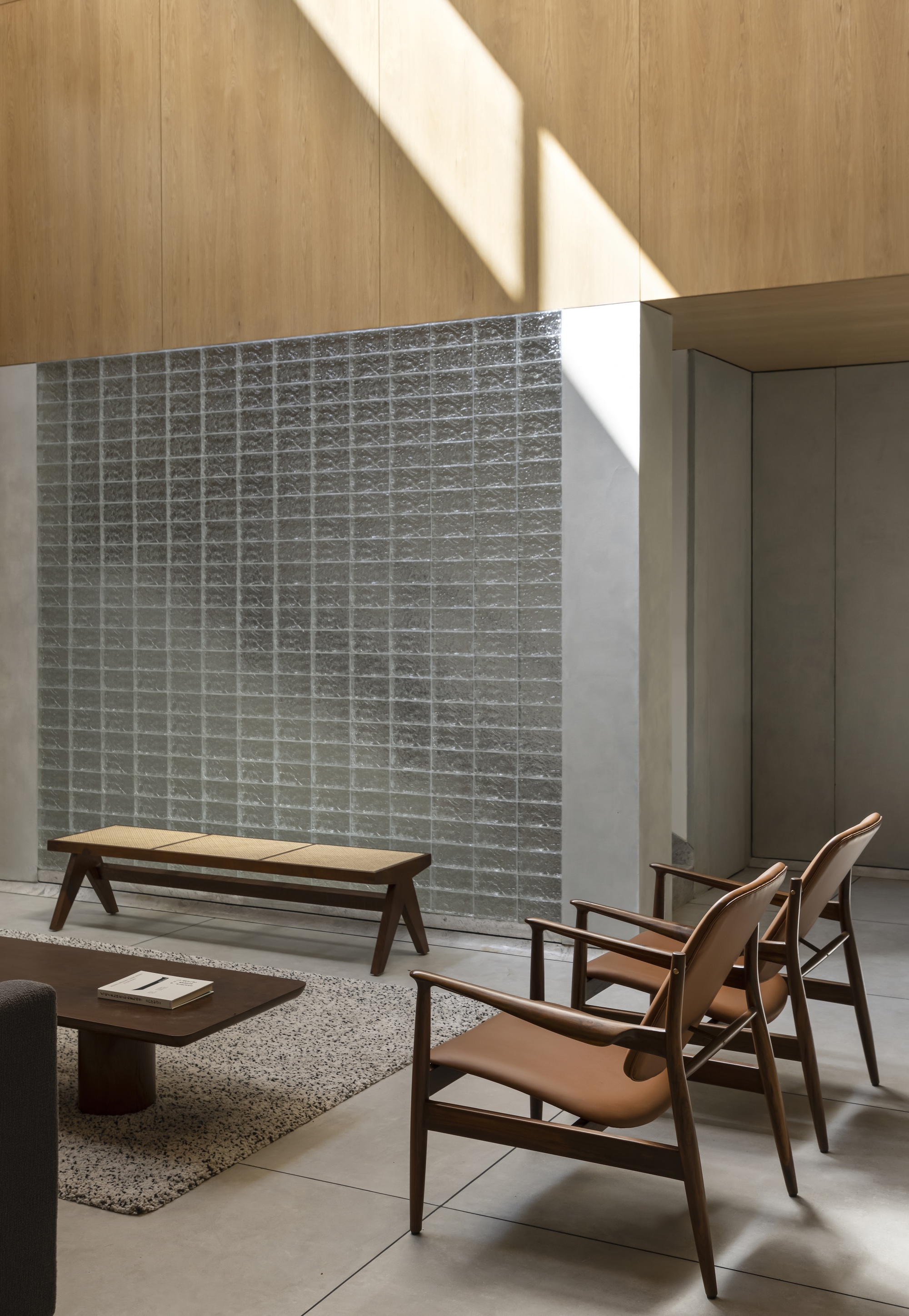Glass block wall beside a wooden bench and leather lounge chairs, with diagonal sunlight cutting across the oak panelled upper wall