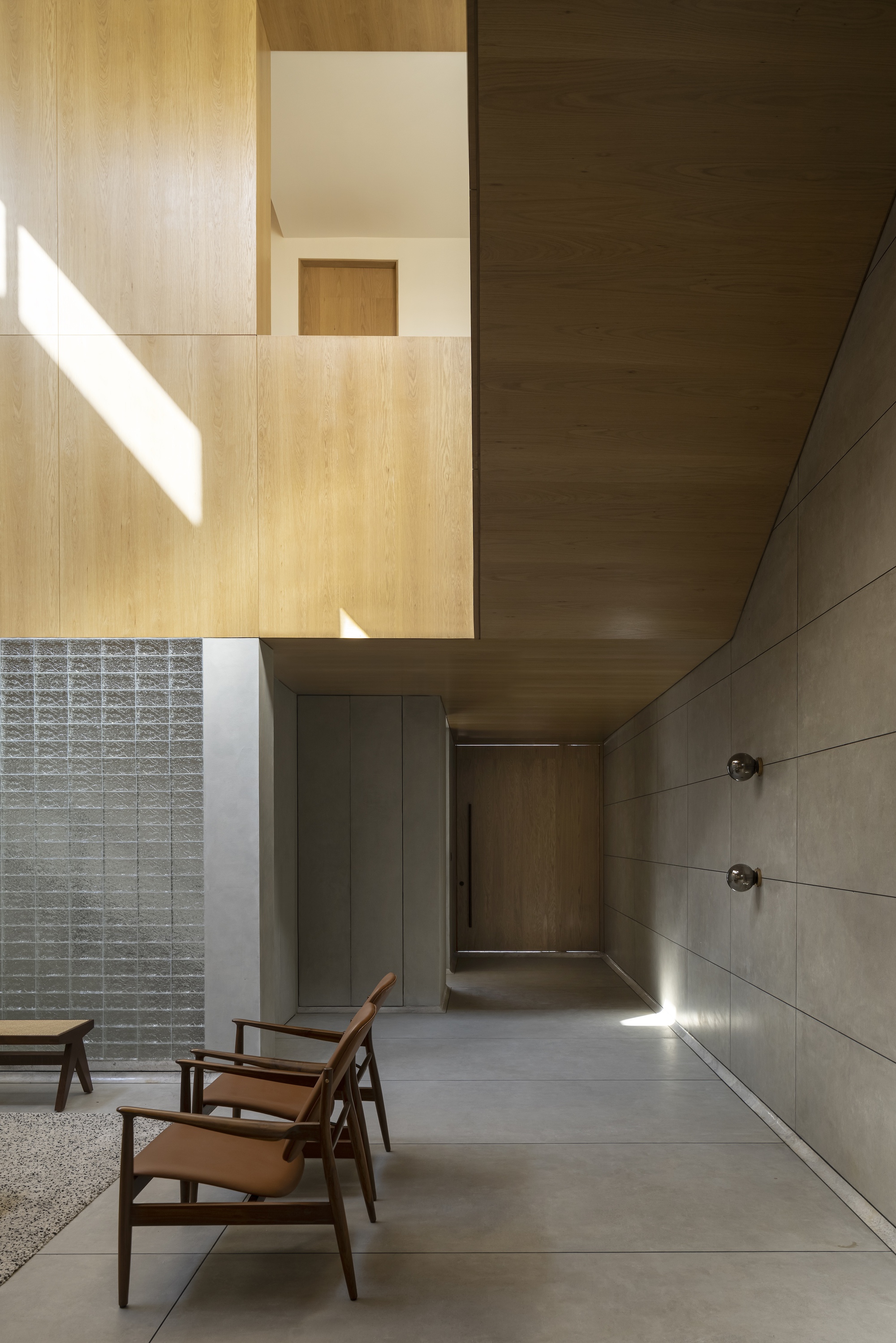Entry corridor with grey panel wall, oak ceiling and wall lights, where a low sun patch lands on the floor