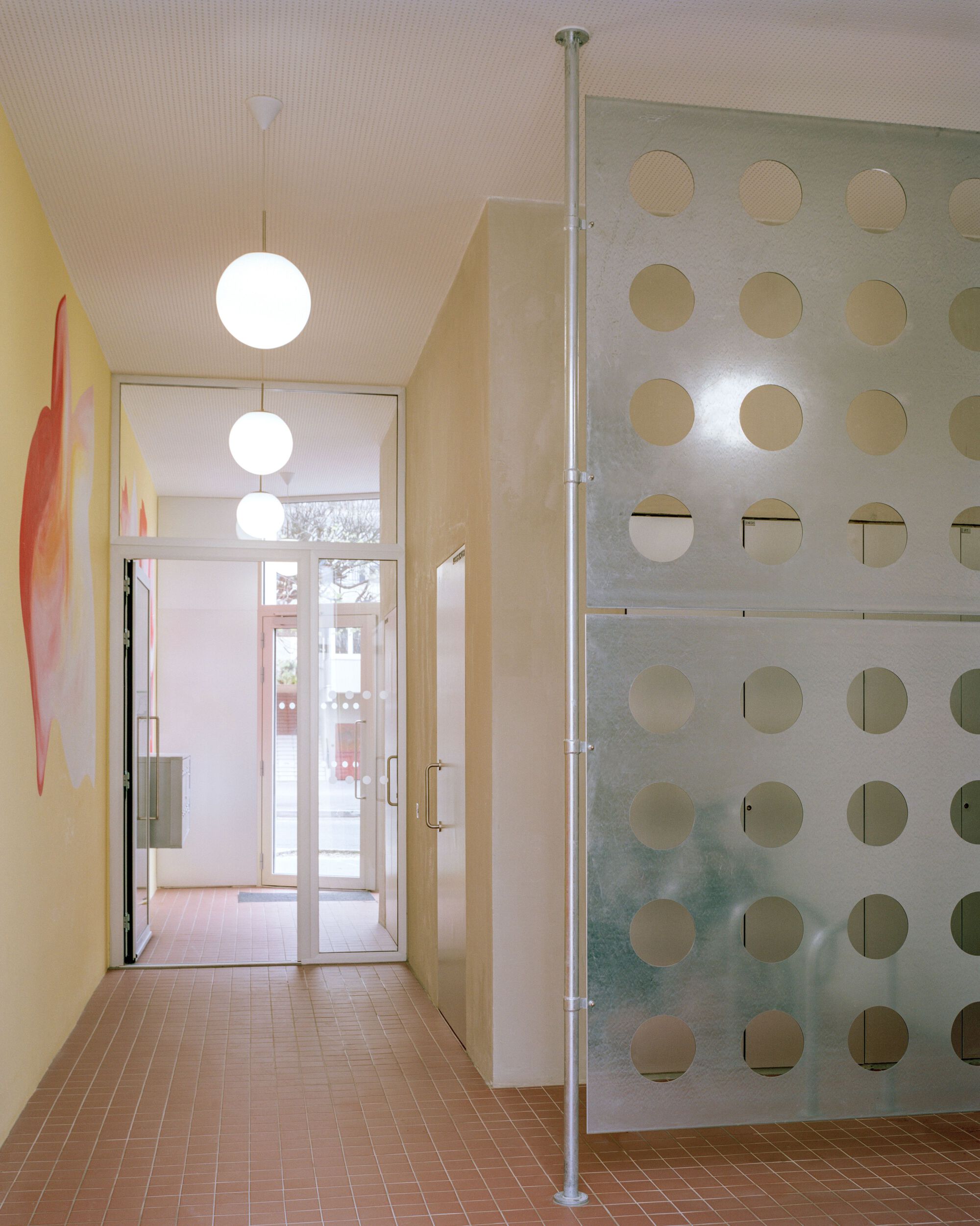 Entrance hall with globe pendant lights, red tile floor and a perforated translucent panel on a slender steel pole
