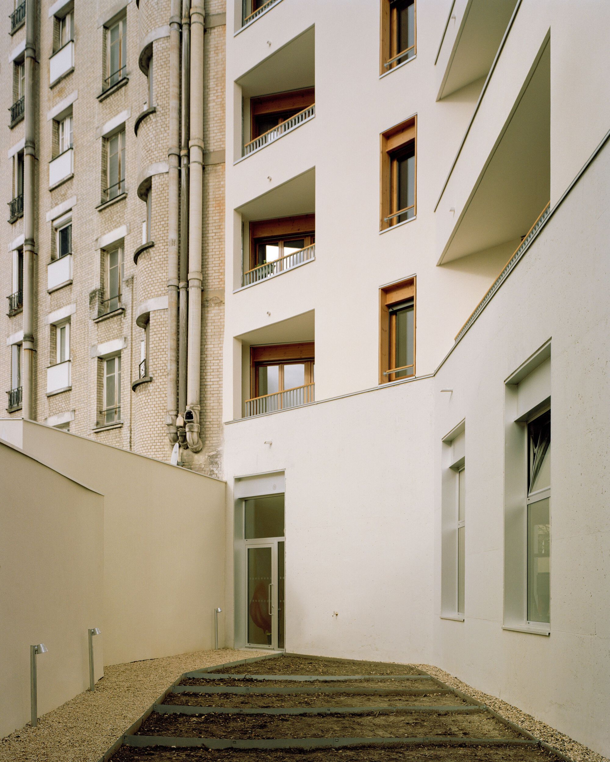 Rear courtyard with a gravel bed and stepped planting, white balconies facing a brick neighbour wall with drainpipes