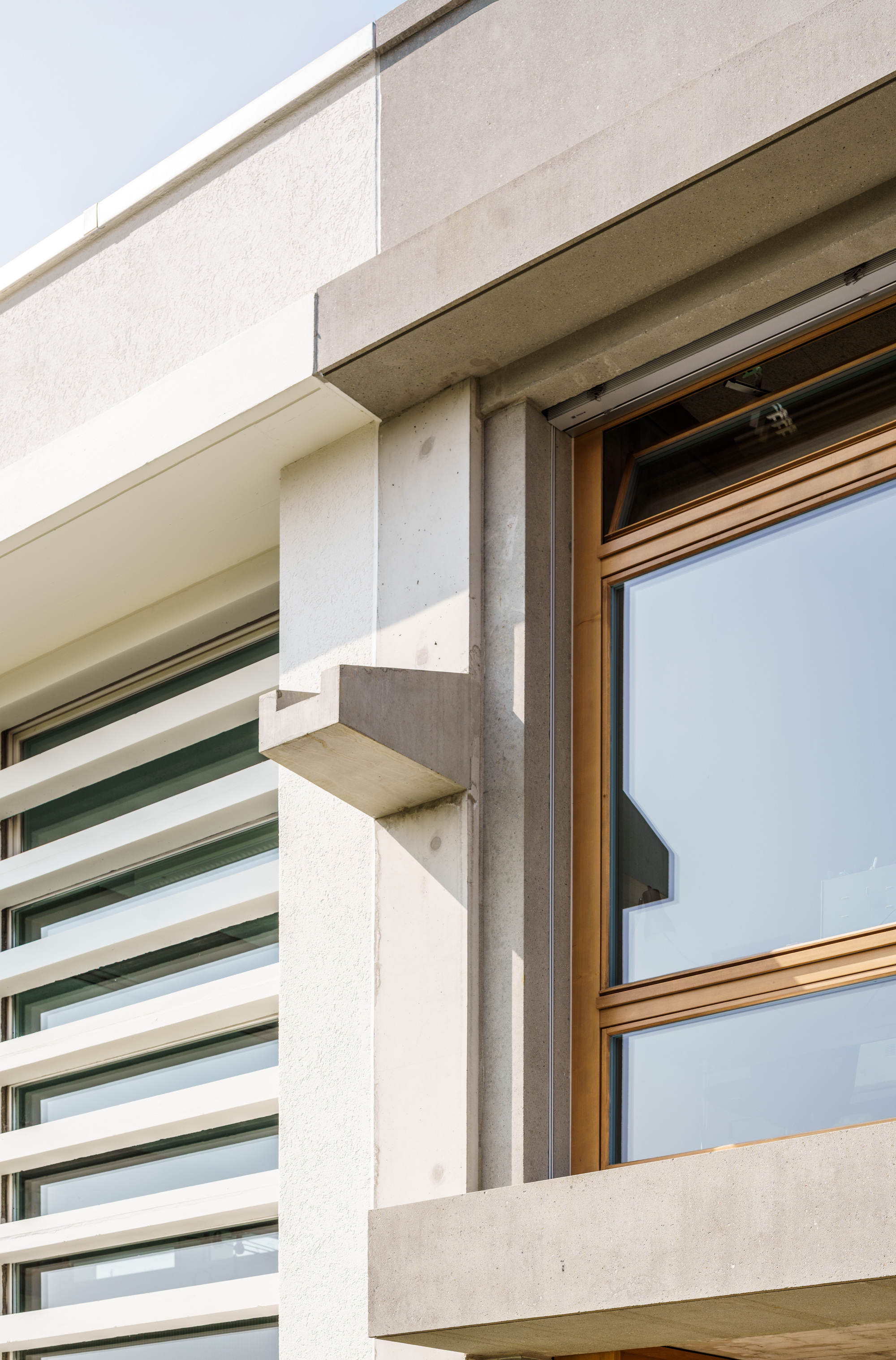 Corner of the concrete facade with a projecting bracket, timber-framed window and horizontal louvres in bright sunlight
