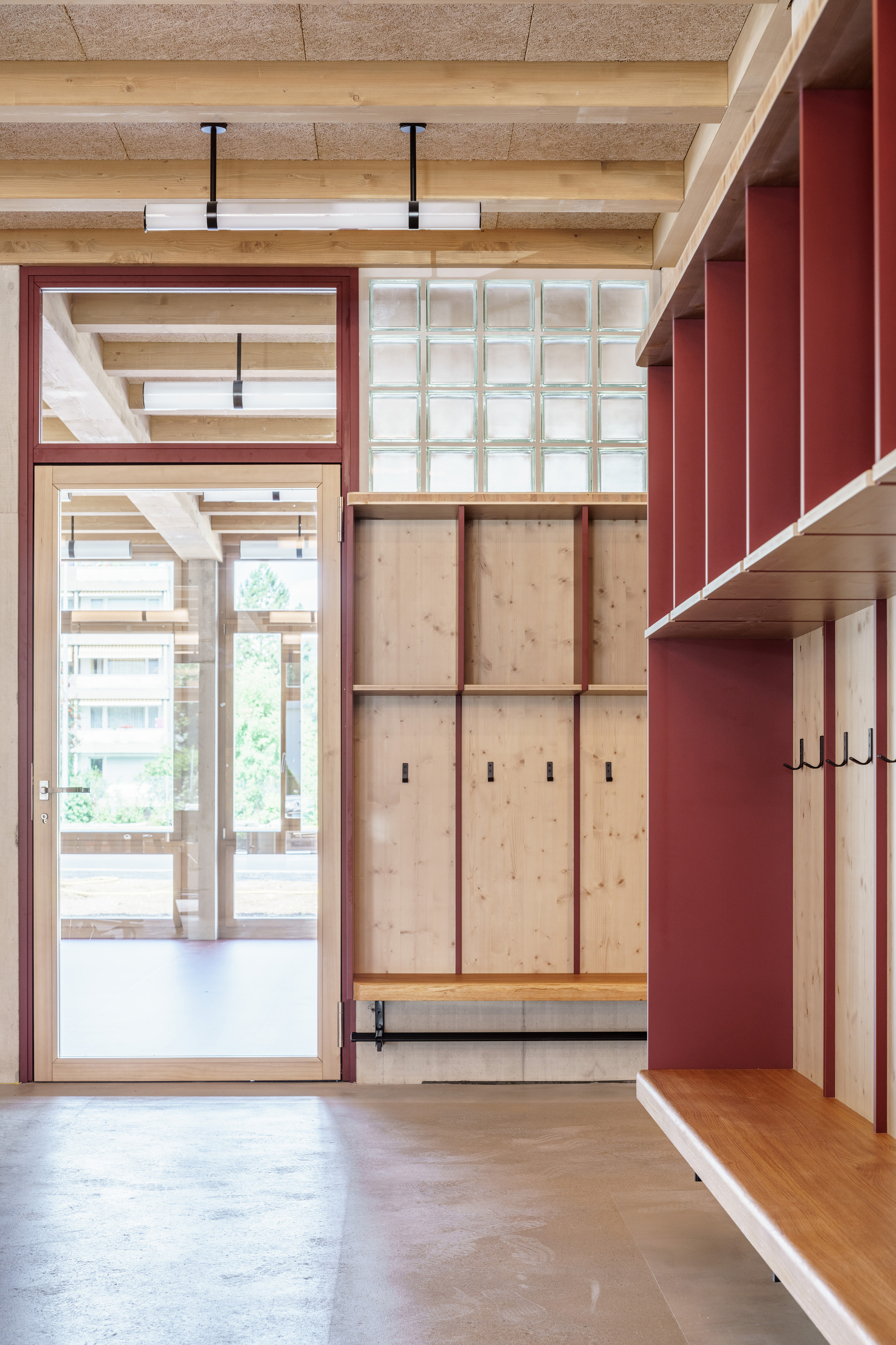 Entrance area with built-in timber lockers, red dividers and coat hooks beside a glazed door and glass block window