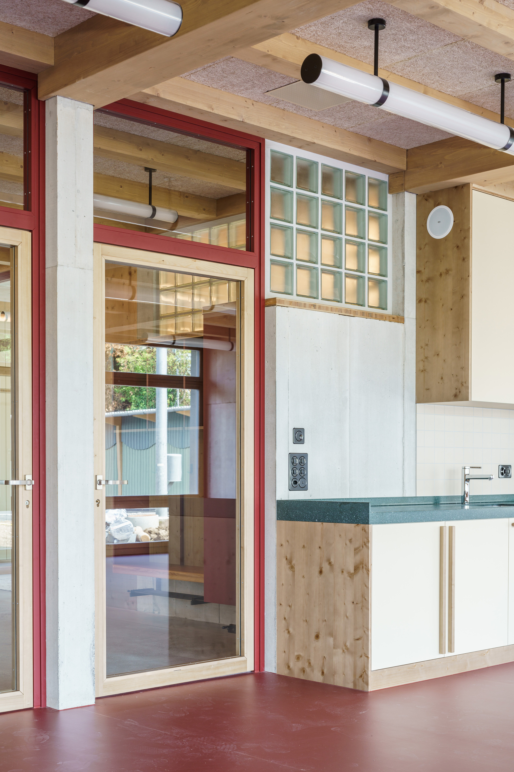 Kitchenette corner with green countertop, glass block window and red-framed timber door above a red floor