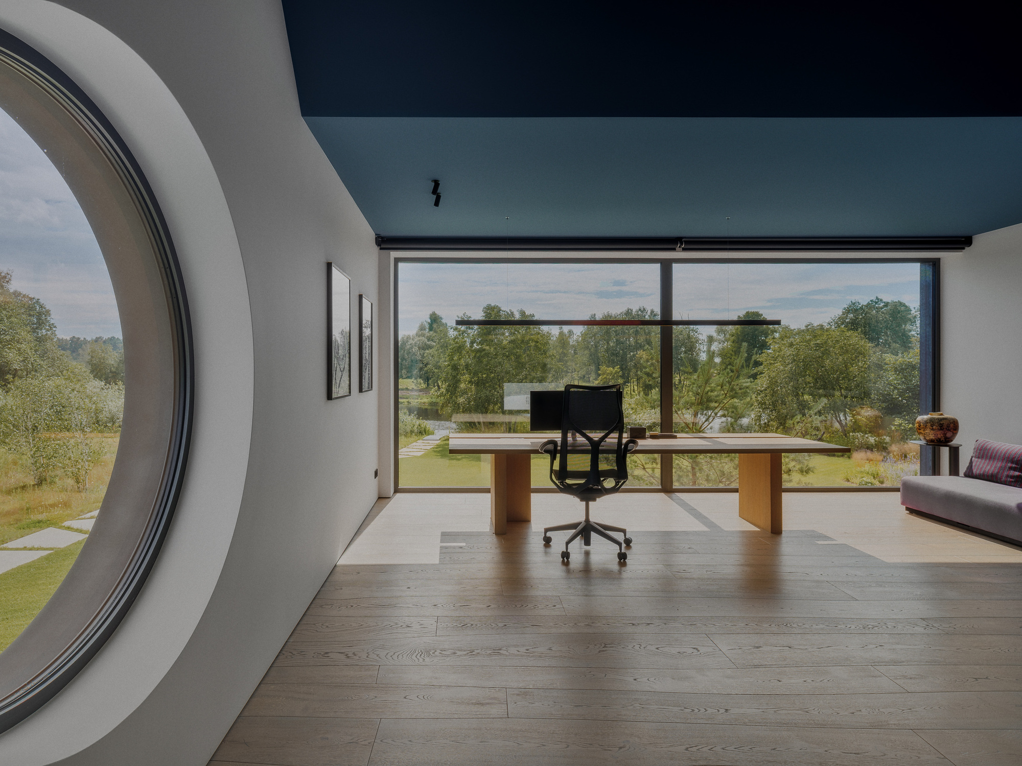 Home office with a wooden desk before a full-height window, a large round window at left and soft daylight on oak floorboards