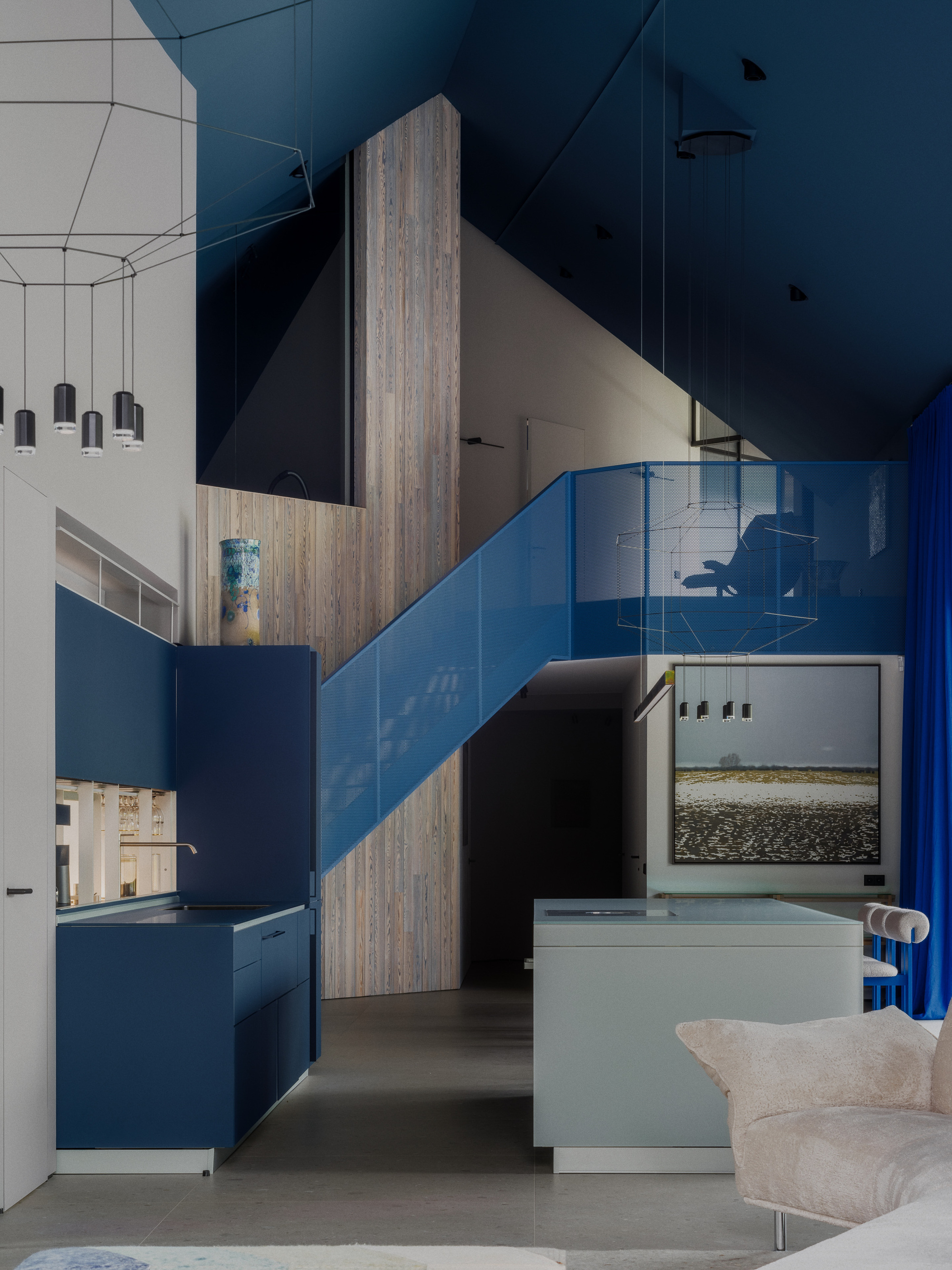 Double-height living space with blue kitchen cabinetry, glass-balustrade stair and weathered timber column under a deep blue sloped ceiling