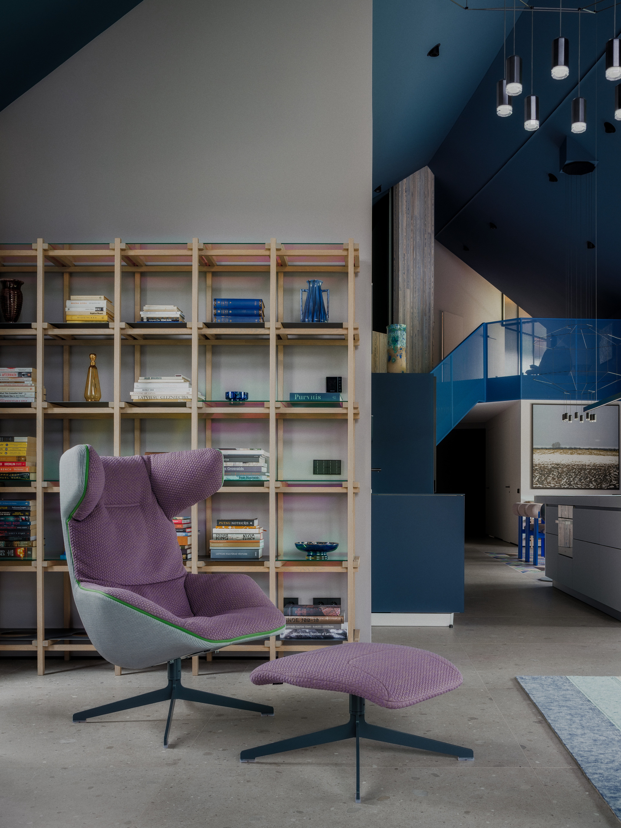 Purple lounge chair and ottoman in front of a timber shelving grid filled with books and glass vessels