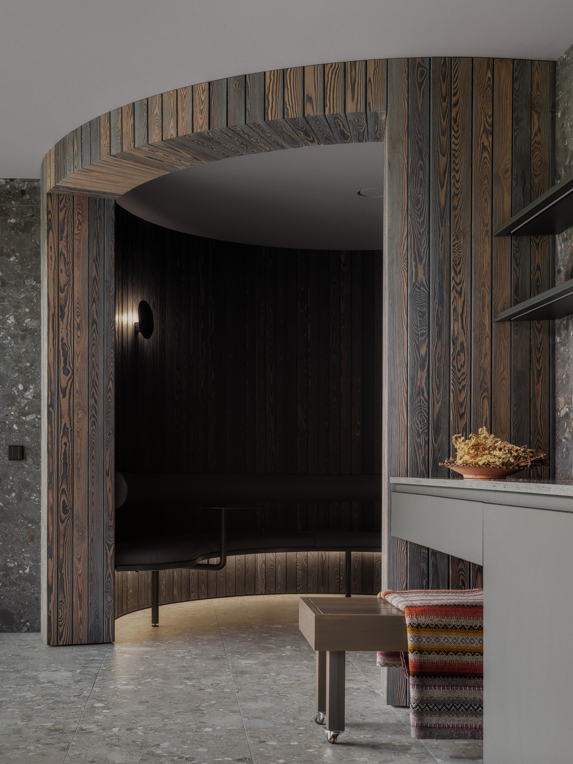 Curved alcove framed by an arch of charred timber boards, with a built-in bench lit from below