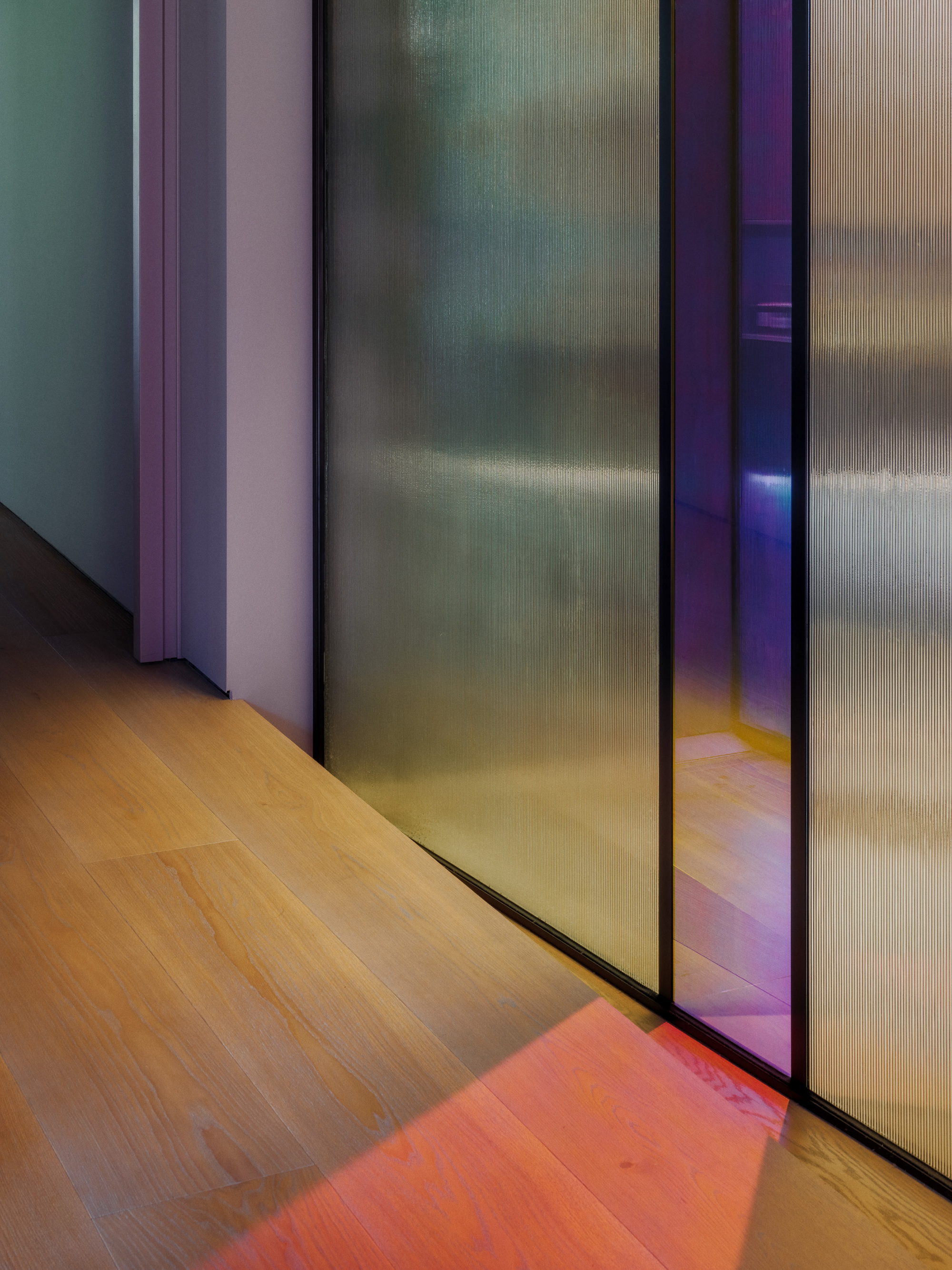 Reeded glass sliding panels in thin black frames beside an oak floor, with a red patch of reflected light