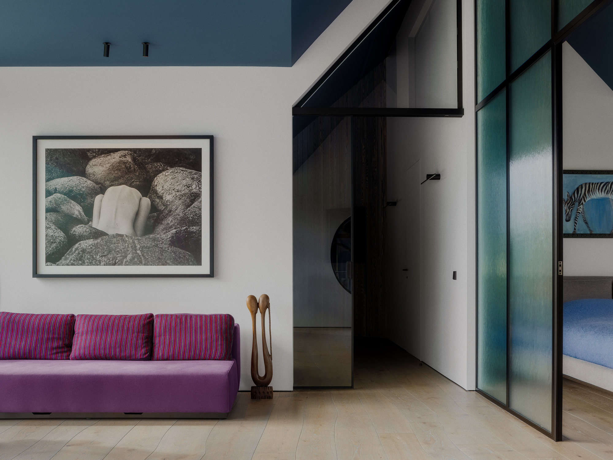 Living room with a magenta sofa under a framed boulder photograph, beside a green reeded glass sliding partition into the bedroom