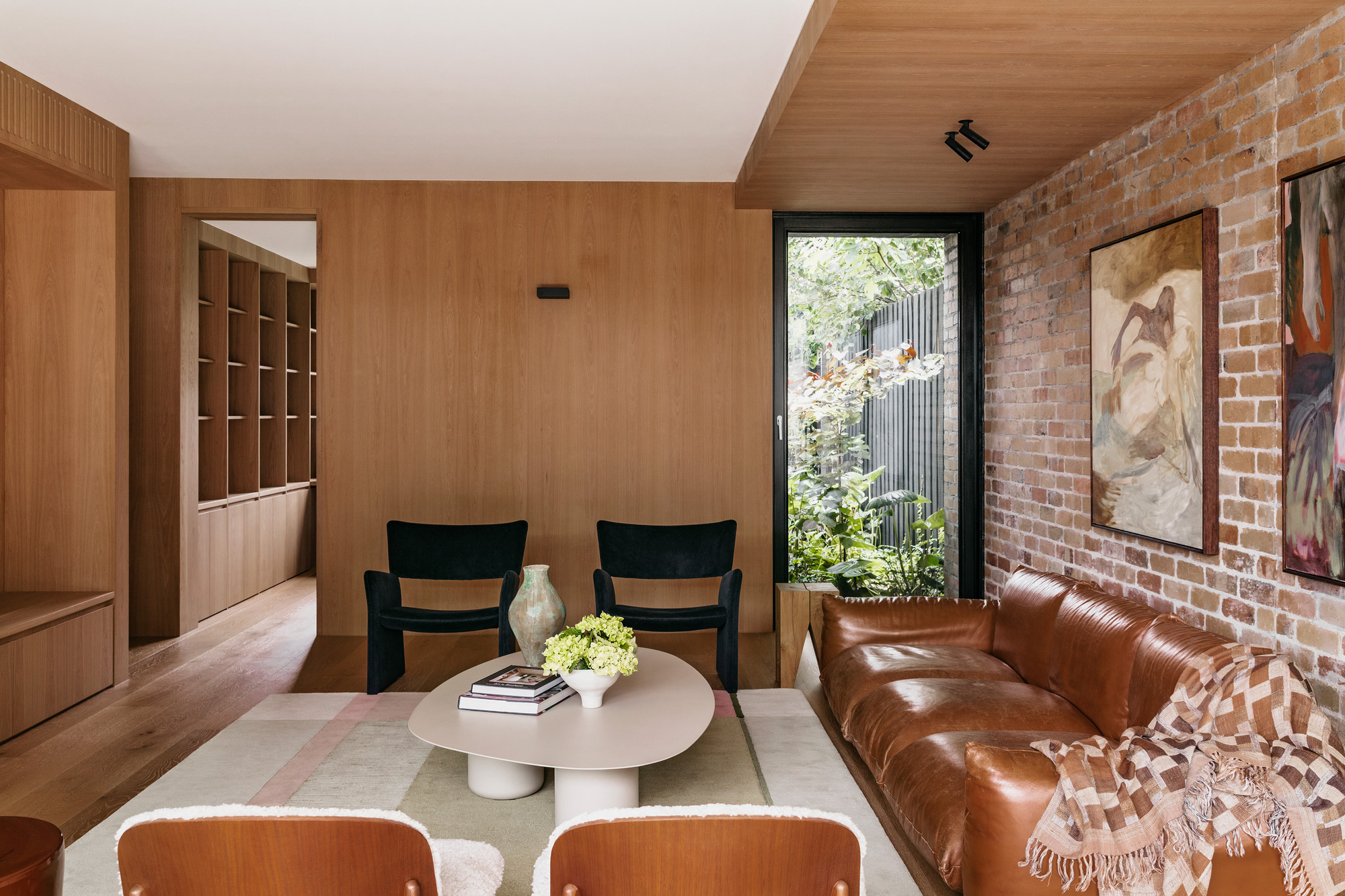 Living room with a tan leather sofa against exposed brick, oak panelled walls and a tall window onto a leafy garden