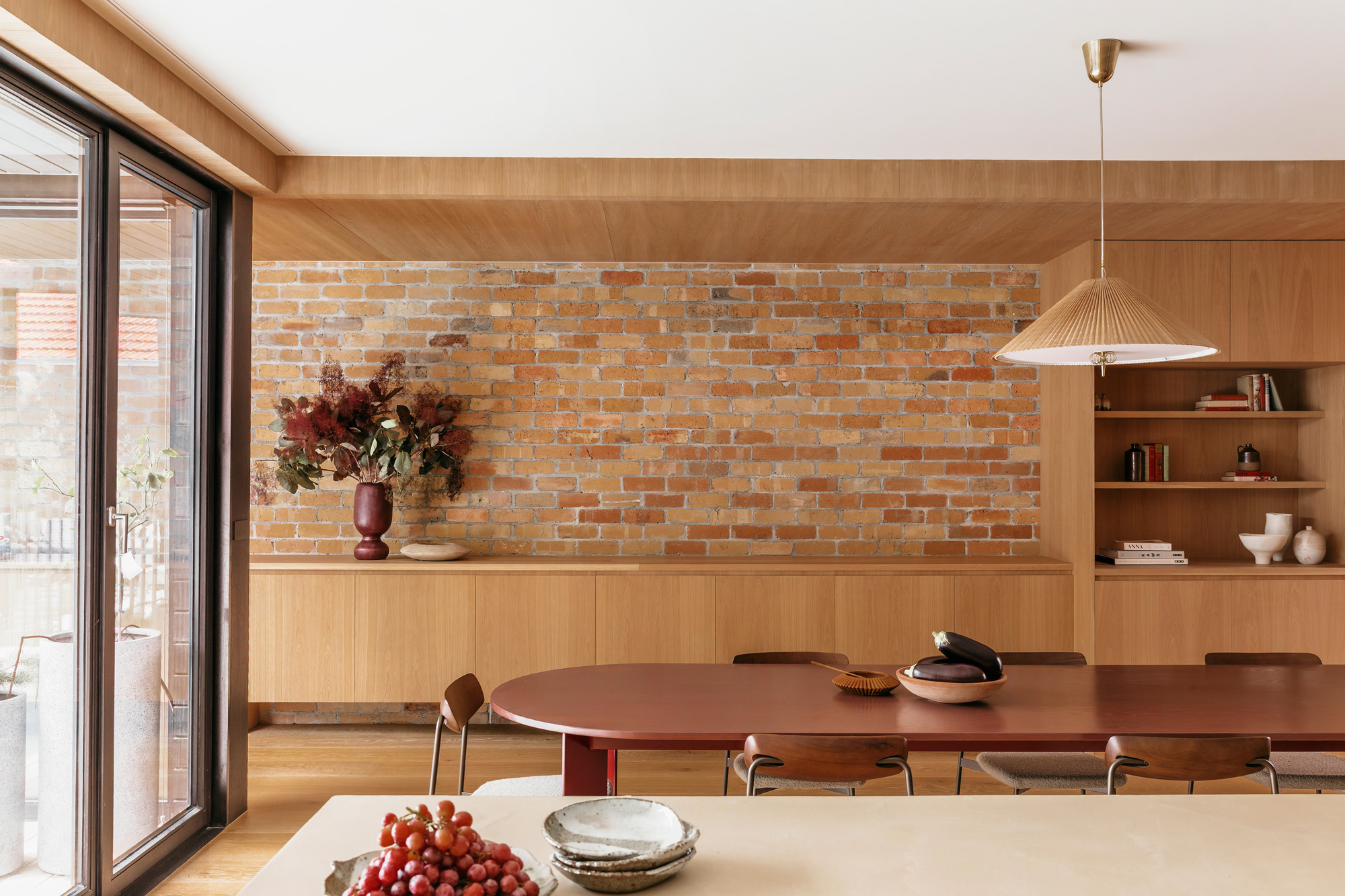 Dining area with exposed brick wall, oak joinery and a red table, daylight coming through the sliding glass door