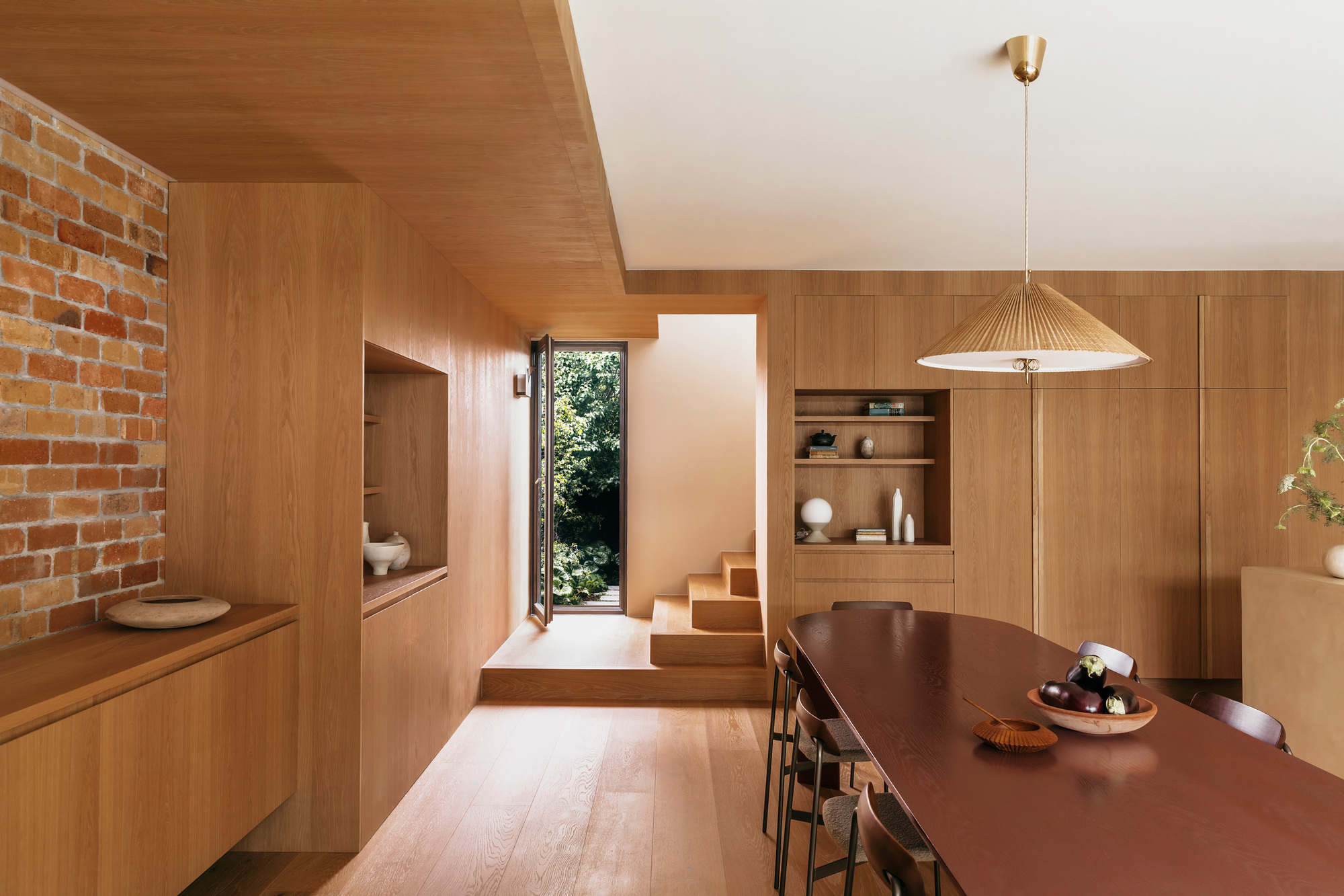 Oak-lined dining room with a pleated pendant light and a short run of steps leading to a green garden door