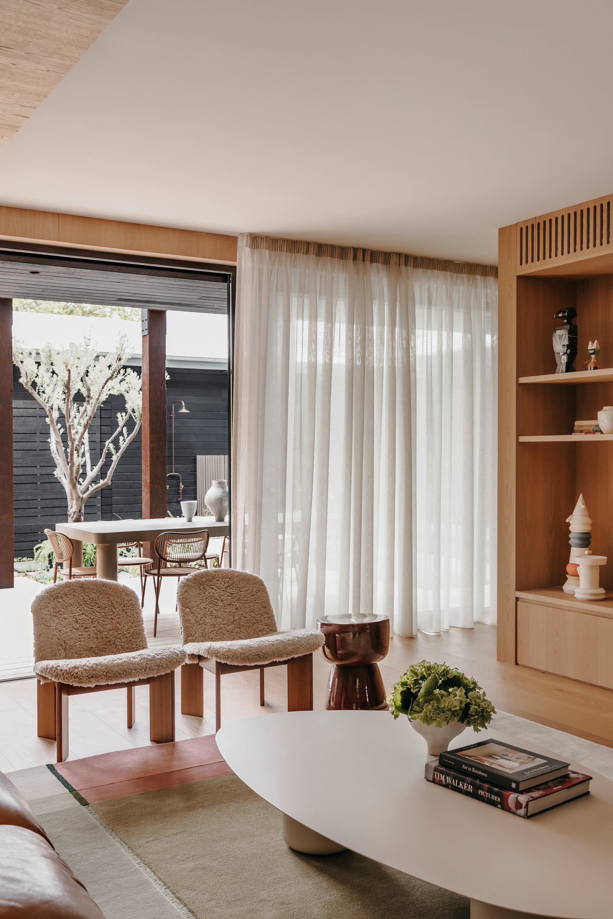 Sheer curtain and shearling chairs in the living area, with a courtyard olive tree visible through open glass doors