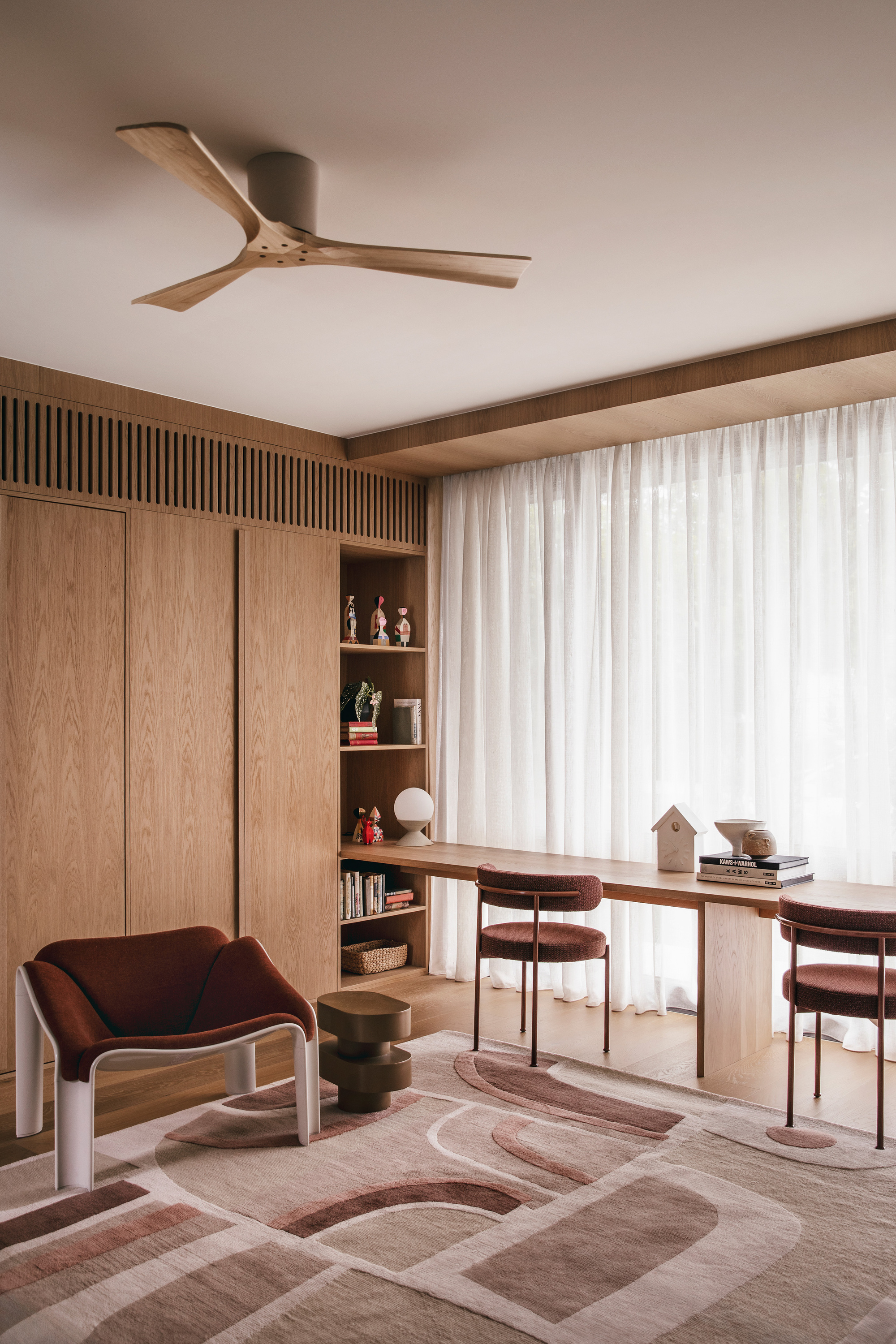 Study corner with a flush ceiling fan, oak cabinet doors, a long desk and a patterned rug in soft daylight