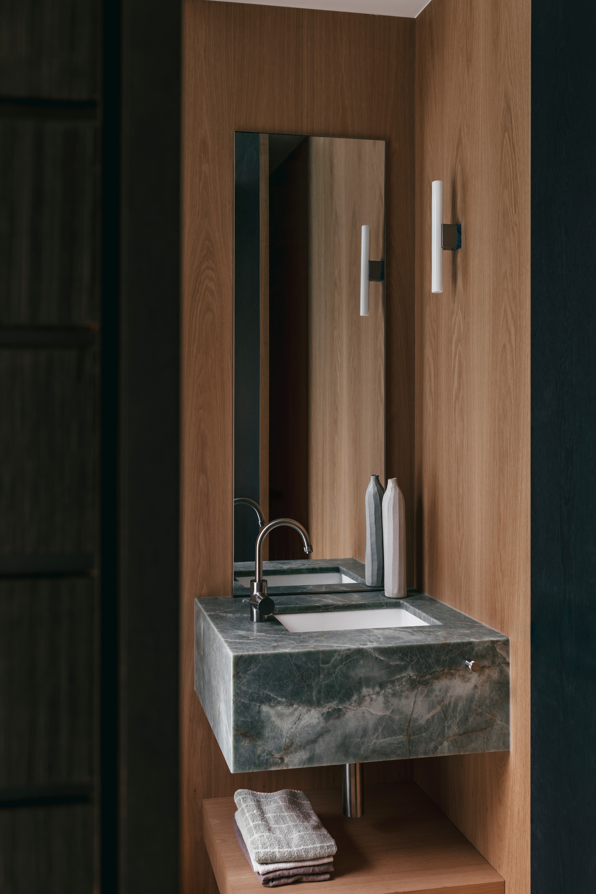 Floating green marble basin with a tall mirror and slim wall lights against oak veneer panelling
