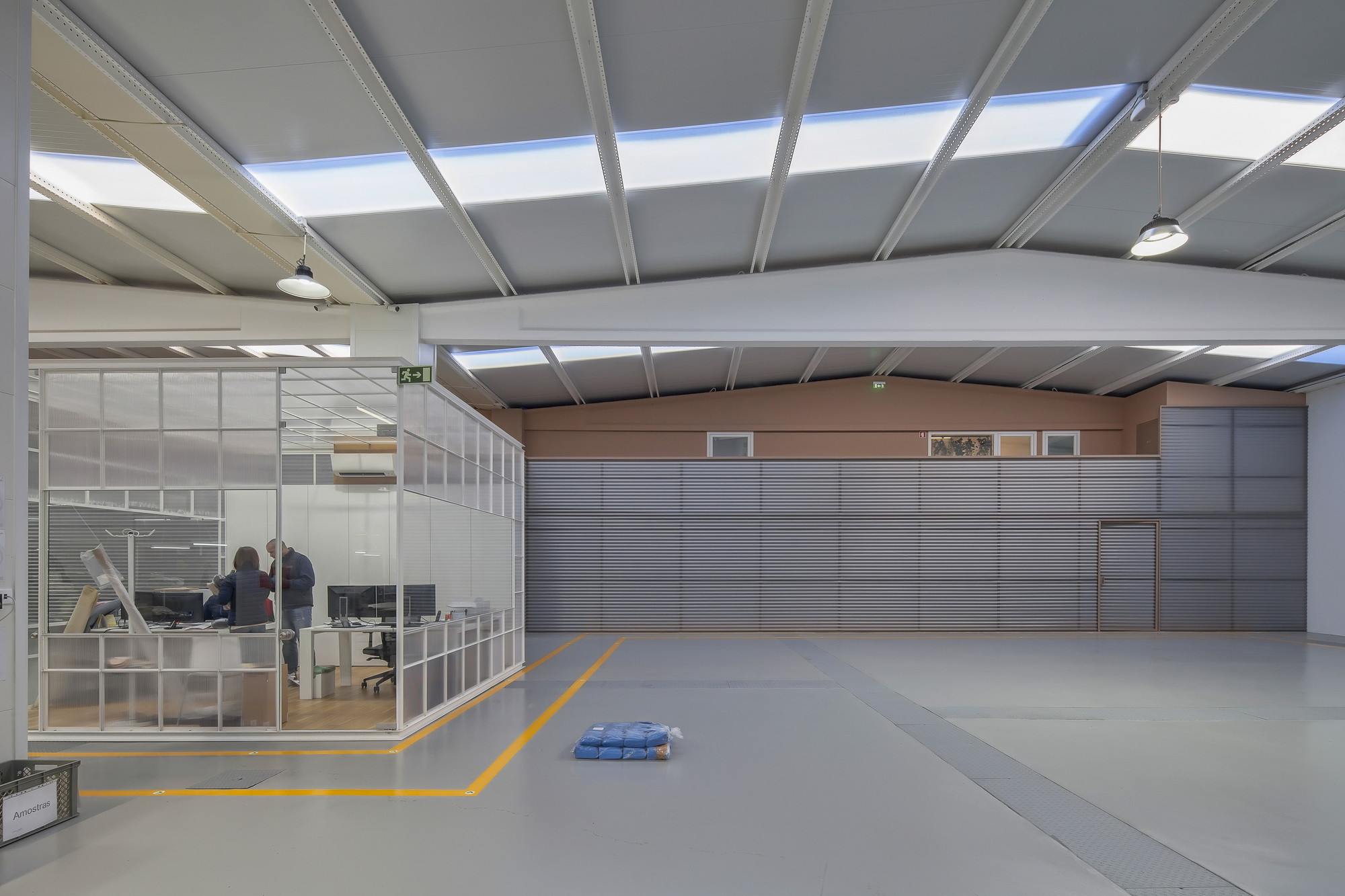 Interior of the production hall with a glazed office cube, yellow floor markings and skylight strips along the pitched ceiling