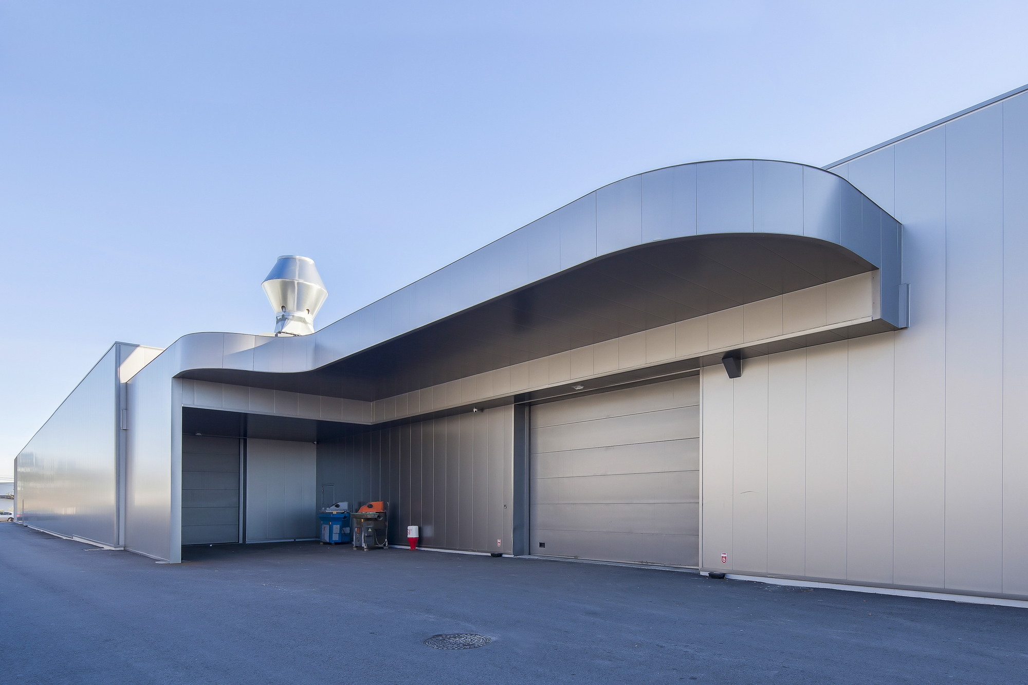 Curved metal canopy over a loading bay with sectional doors and a rooftop vent under a pale dusk sky