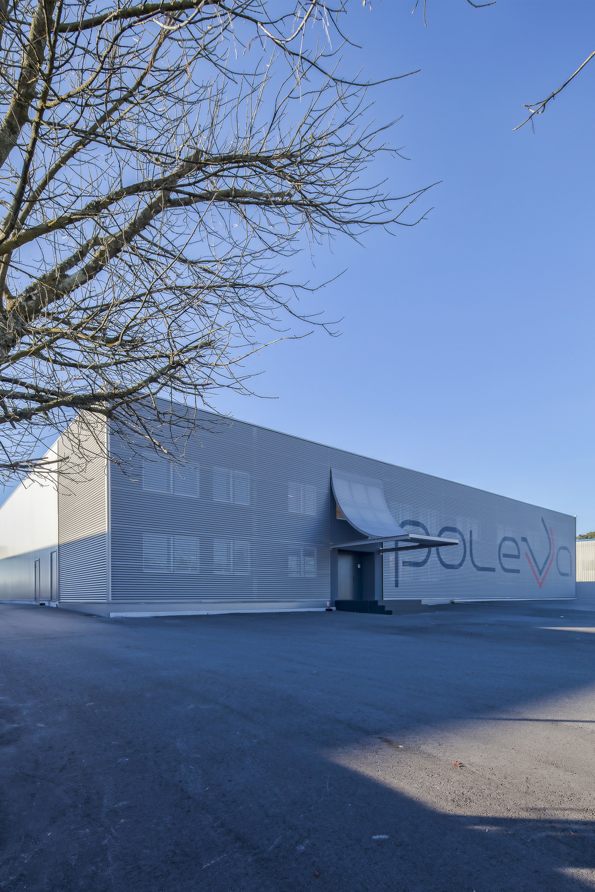 Corrugated metal facade with a curved entrance canopy and painted lettering, framed by bare branches in winter light