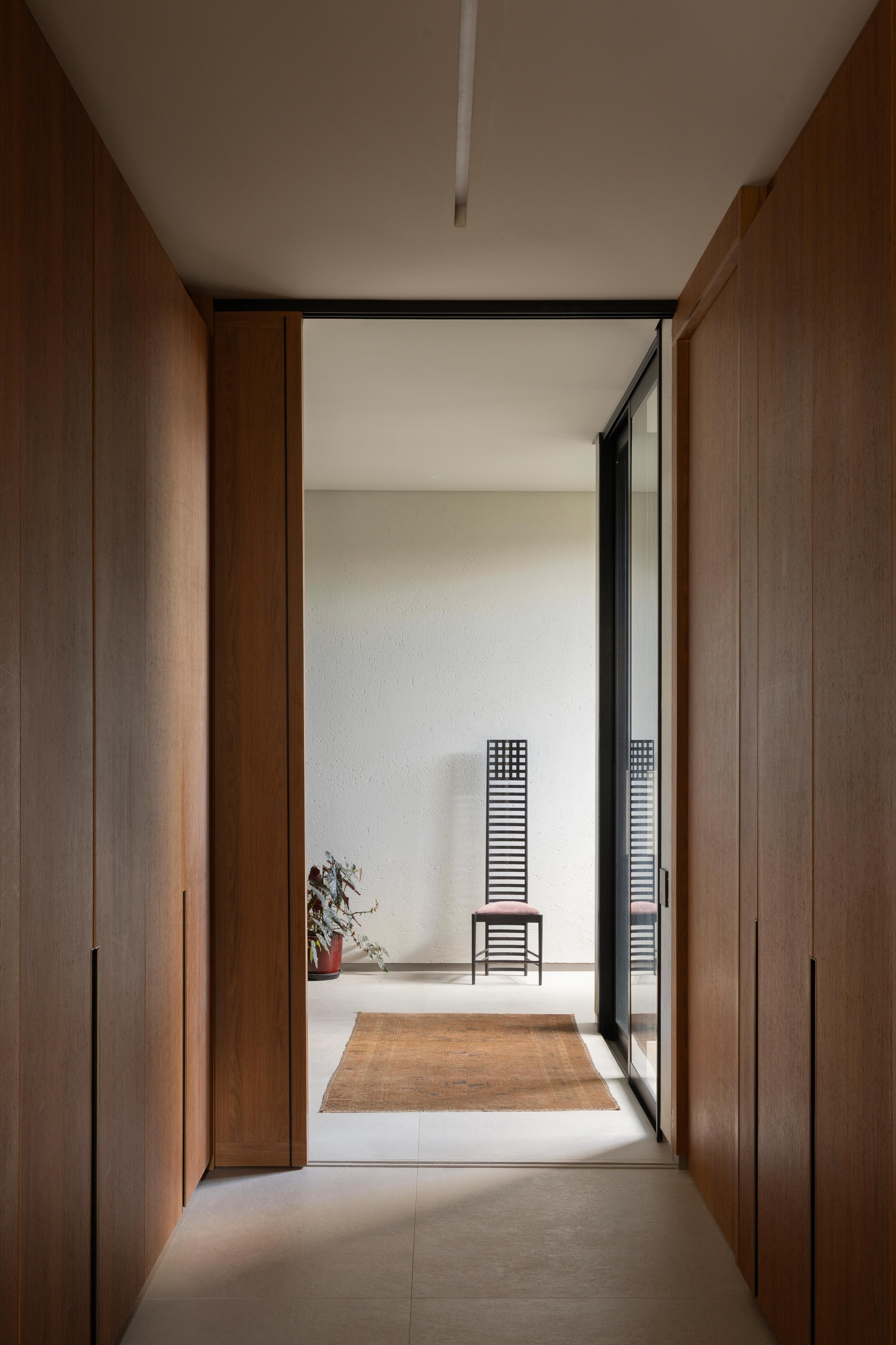 Corridor lined with timber panel doors opening to a tall lattice-back chair and a worn rug in soft daylight