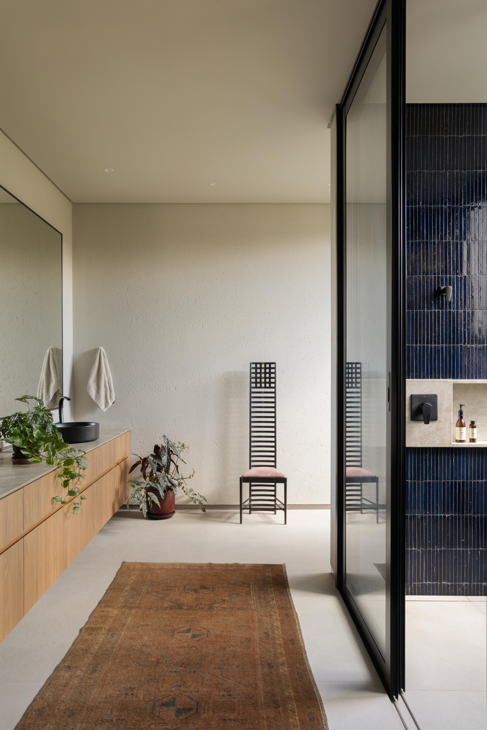 Bathroom with a timber vanity and black basin, a lattice-back chair, a faded runner and a glass-enclosed shower with navy tiles