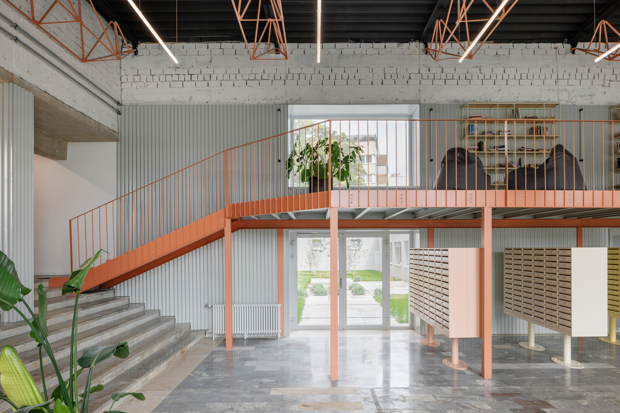 Lobby with a coral steel mezzanine, stair and mailboxes beneath exposed brick, with a potted plant in the foreground