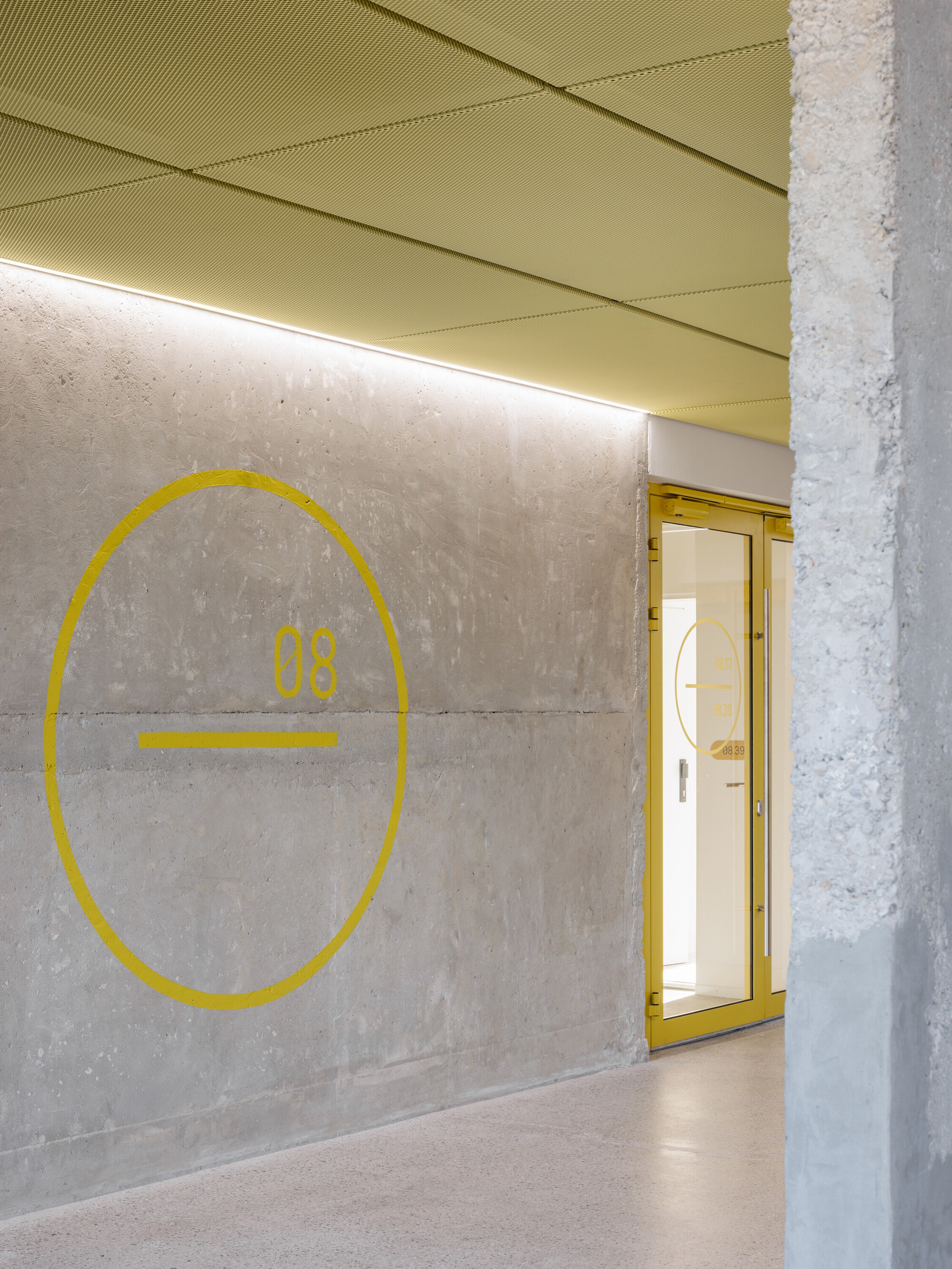 Yellow circle and number 08 painted on a board-marked concrete wall beside a yellow-framed glass door